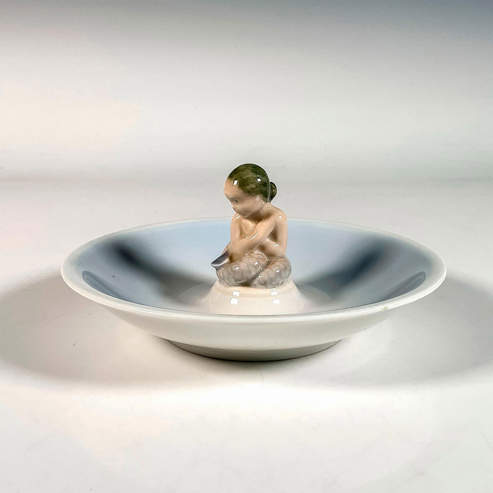 Royal Copenhagen Mermaid Dish: Art nouveau decorative dish with figure depicting a baby mermaid sitting in the center. Royal Copenhagen backstamp. Artist: Hans Henrik Hansen Issued: c. 1952 Dimensions: 6"W x 3.25"H Manufacturer: Ro
