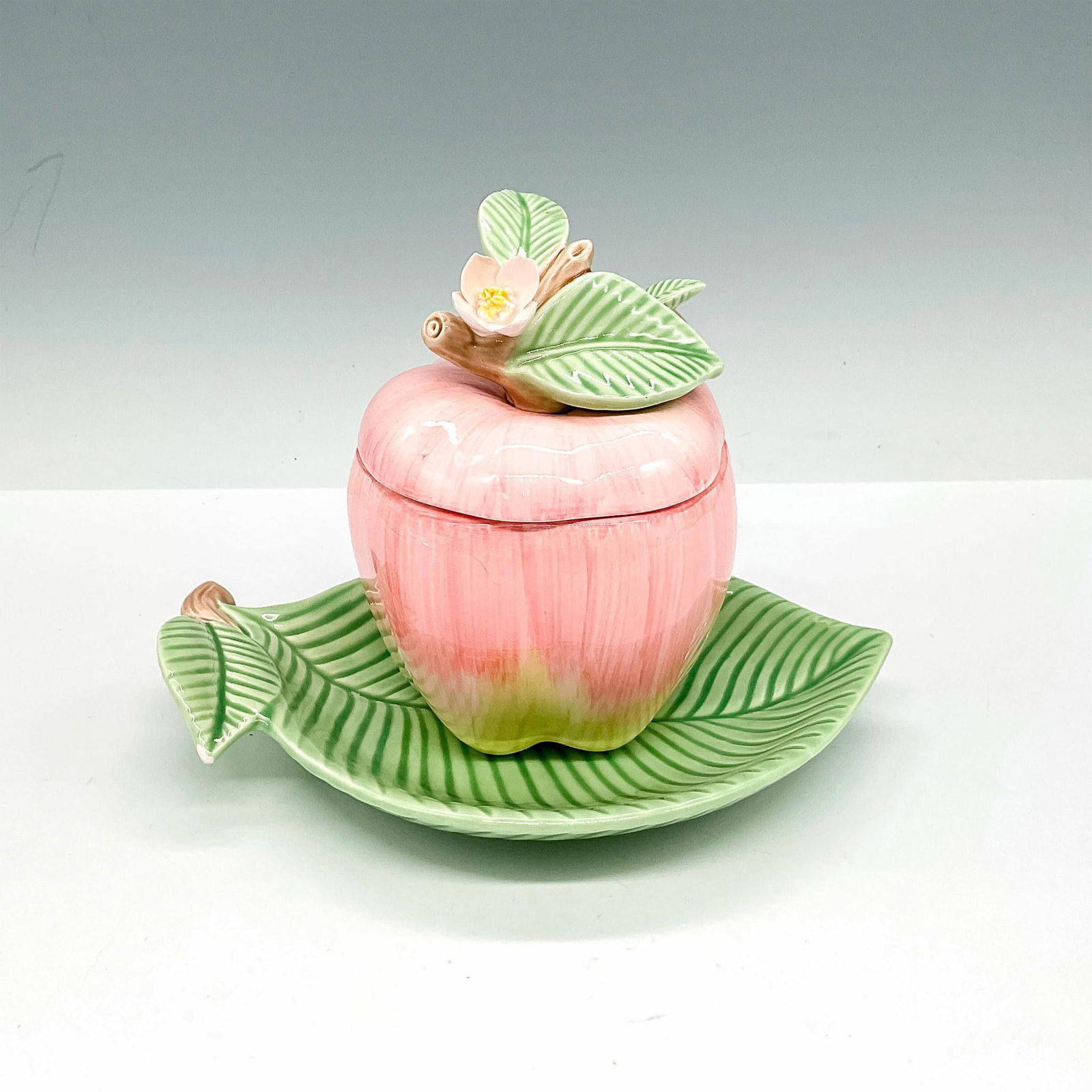 Fitz and Floyd Jam Pot with Saucer, Apple: Hand-painted jam pot modeled as a red apple with stem and white flower. Includes a green leaf-shaped saucer and spoon modeled into the shape of a stem. Fitz and Floyd Inc. backstamp. Jam pot measureme
