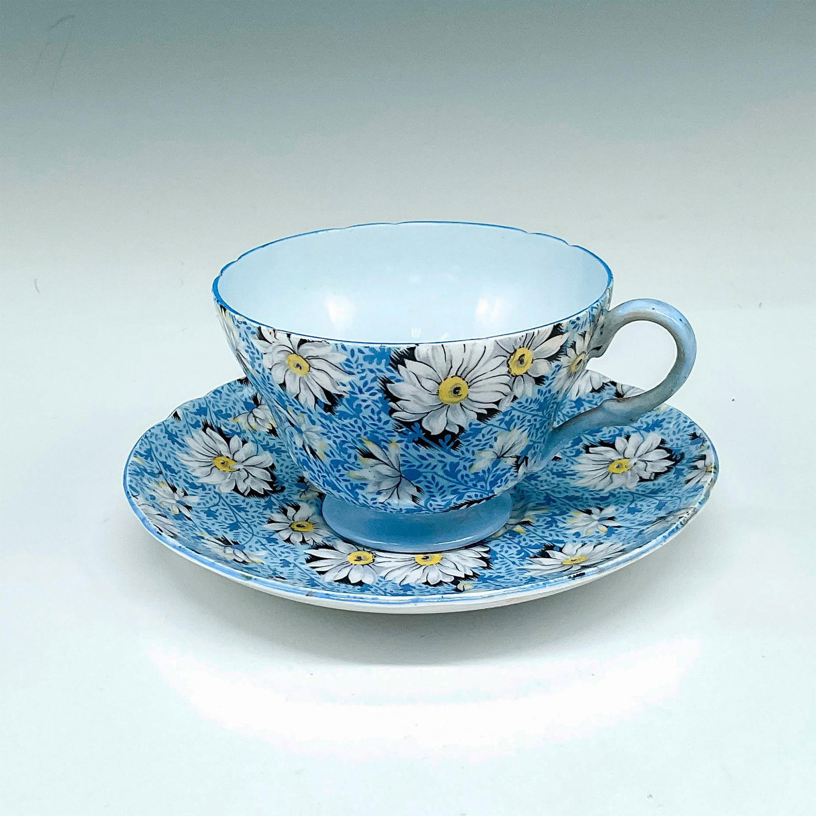 2pc Shelley Bone China Teacup and Saucer, Blue Daisy: Beautiful blue dappled pattern with daisies throughout design. Blue rim, base and handle offset design. Set includes teacup 2.5"H x 3.5"dia. and saucer 0.75"H x 5.75"dia. Shelley England backstamp. Is