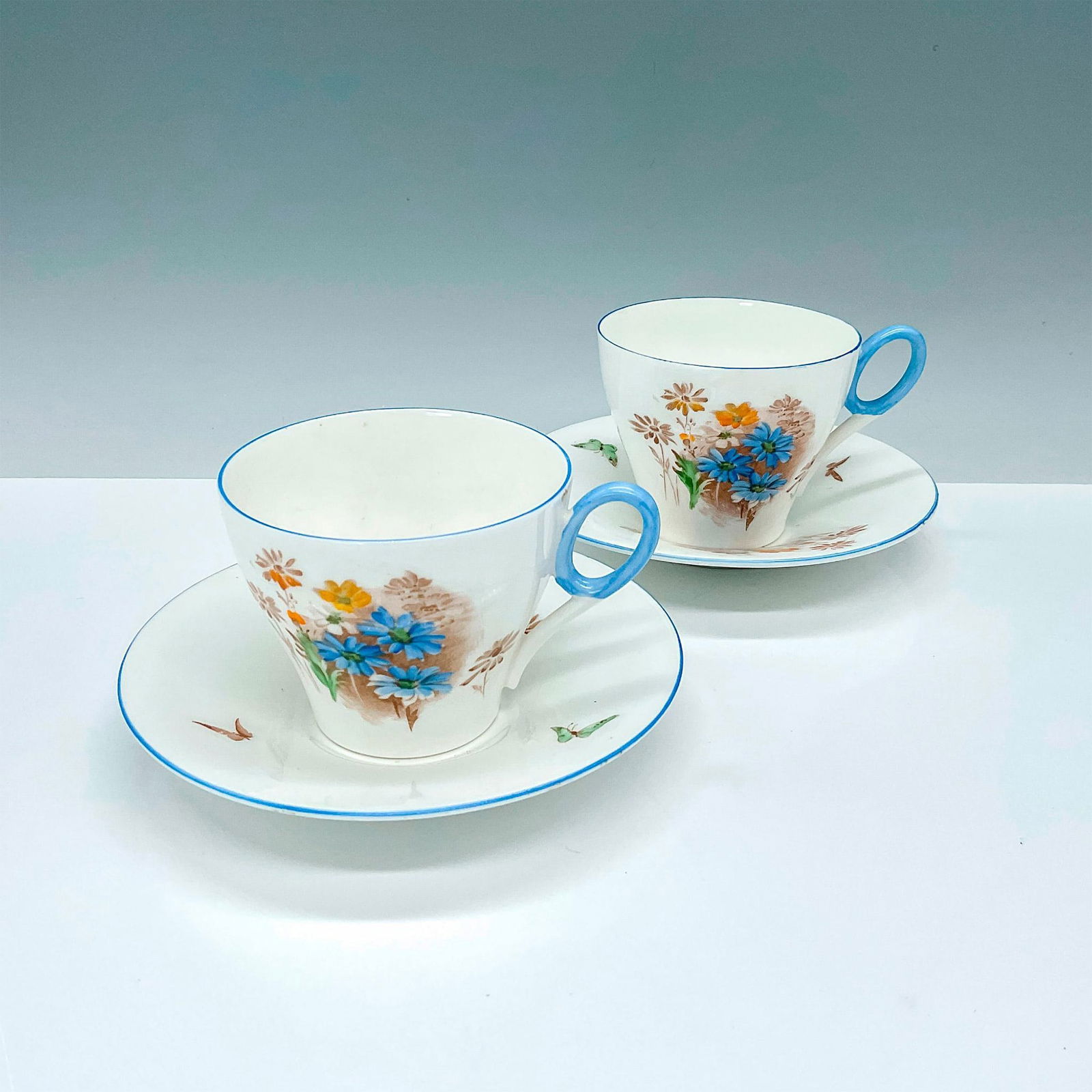 4pc Shelley China Teacups and Saucers Pattern 795072: 2 beautiful white bone china teacups with matching saucers decorated with blue flowers, brown accents and blue trim. Shelley backstamps. Cup: 4.25"L x 3.5"W x 2.75"H. Saucer: 1"H x 5.75"dia. Issued: 2