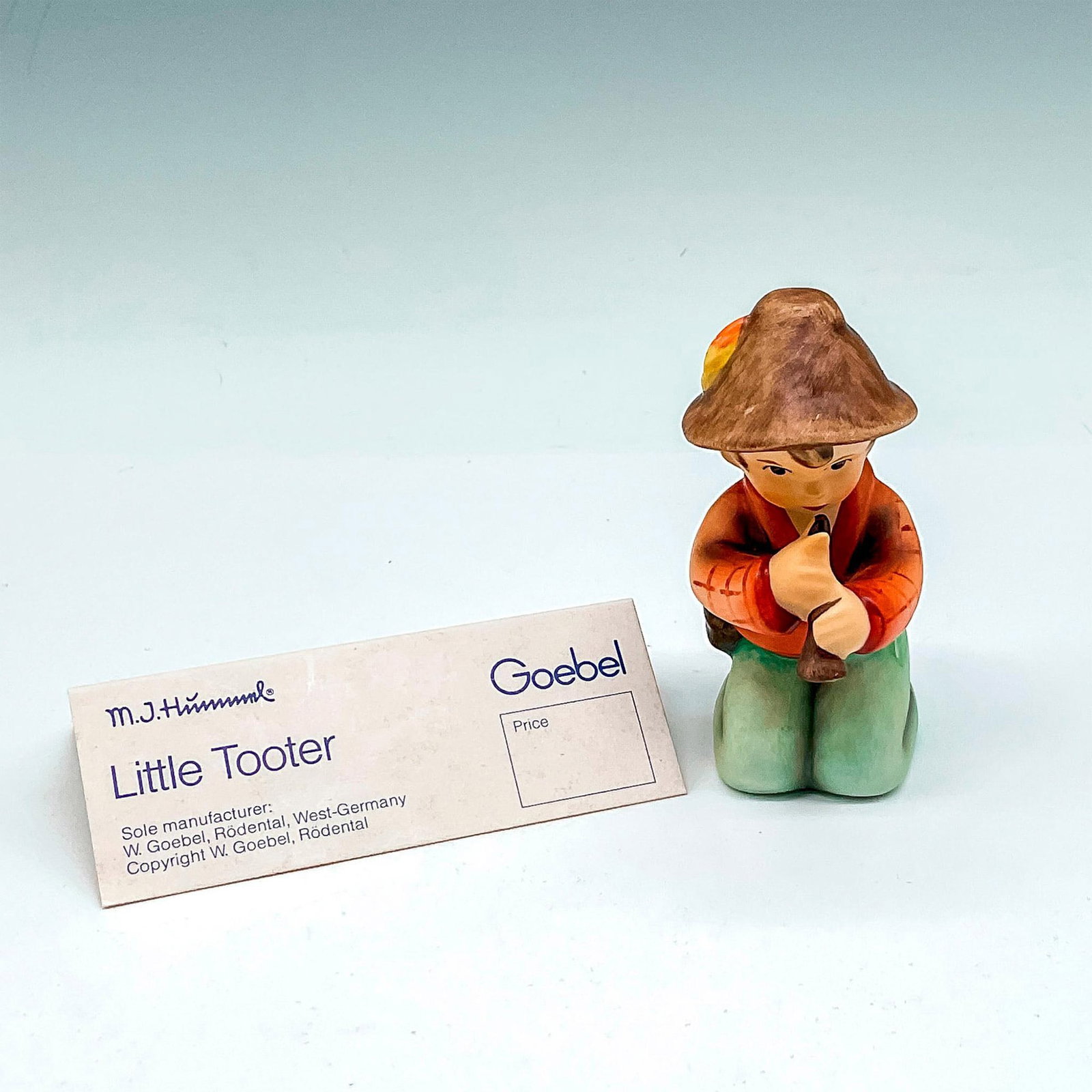 Goebel Hummel Porcelain Figurine, Little Tooter: Matte finished kneeling figural with instrument. Colored in brown, orange and green. Goebel backstamp. 214H. This item has its original box: 3.75"L x 5.5"W x 4"H. Certificate of Authenticity included.