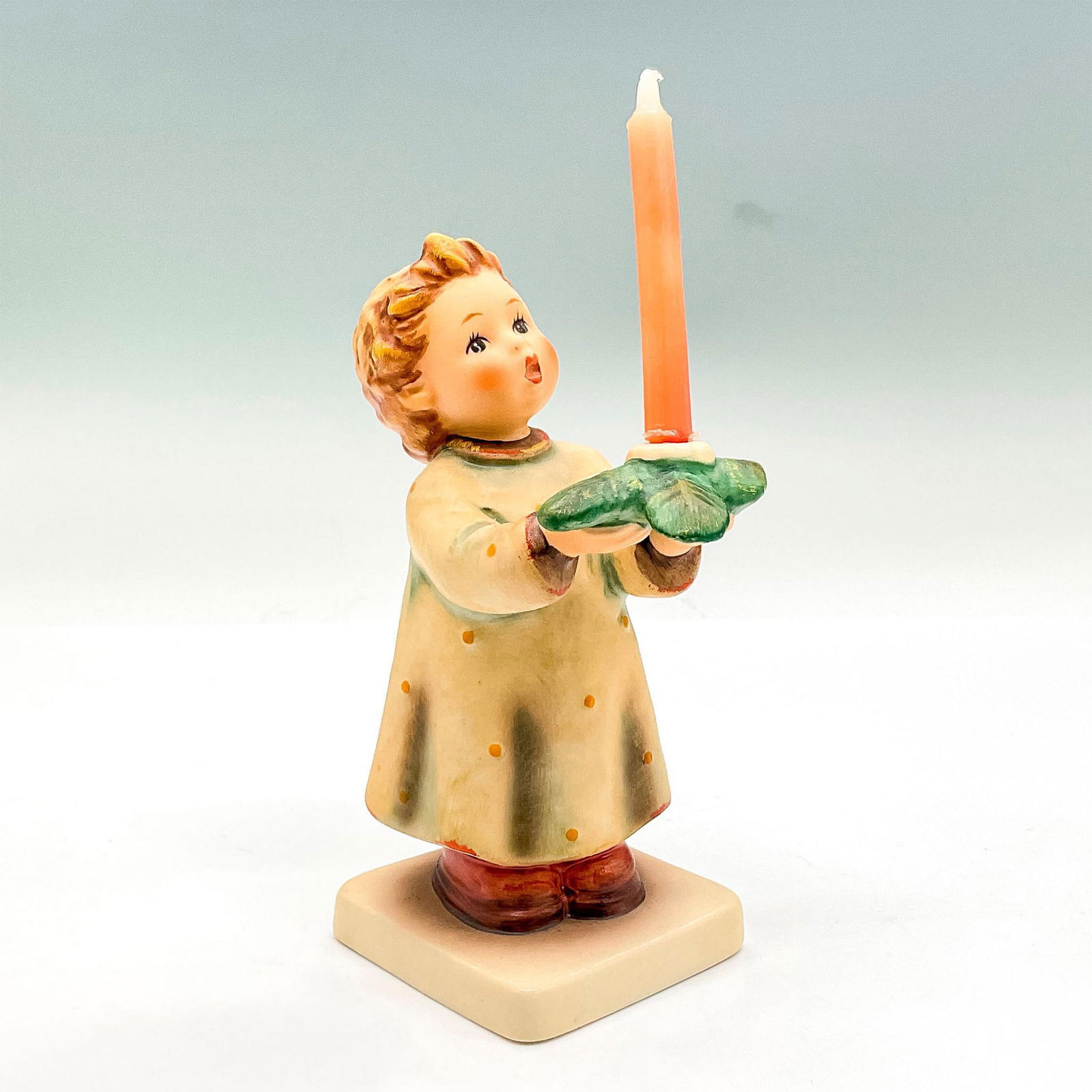 Goebel Hummel Porcelain Figurine, A Gentle Glow HUM 439: Hand painted figure of a young boy holding a candlestick decorated with leaves. Goebel backstamp. This item has its original box: 7.5"L x 5.25"W x 4"H. Certificate of Authenticity included. Dimensions