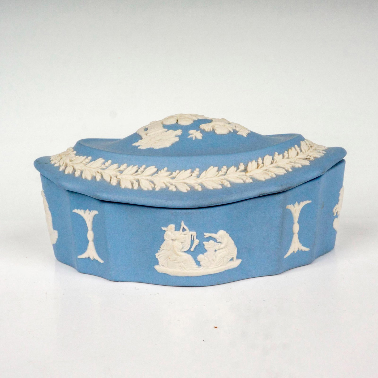 Wedgwood Jasperware Lidded Box: Light blue ground decorated in a relief depicting neoclassical scenes with a band of foliage surrounding the lid. Wedgwood Made in England backstamp. Issued: 20th c. Dimensions: 4.25"L x 3"W x 2.25"H