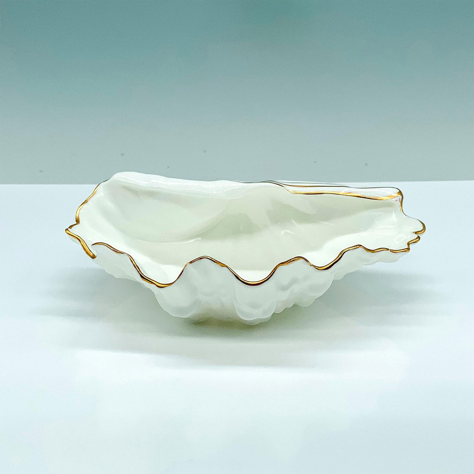 Wedgwood Bone China Oyster Shell Trinket Box: A white trinket box in the shape of half of an oyster shell with gold-colored line accents around the borders. Wedgwood backstamp. Dimensions: 5.75"L x 4.5"W x 2"H Manufacturer: Wedgwood Country of Or