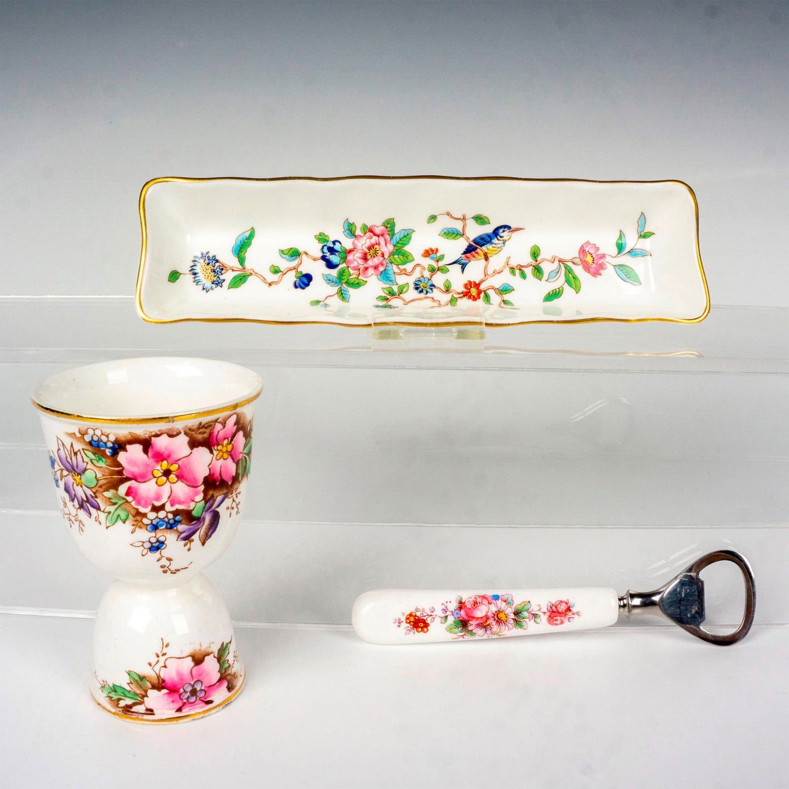 3pc Floral Ceramic Grouping, Aynsley & Melba: This grouping includes a double cup egg cup crafted from Melba, a ceramic handled bottle opener decorated with a floral pattern, and the complimentary Aynsley rectangular tray in the Pembroke pattern.