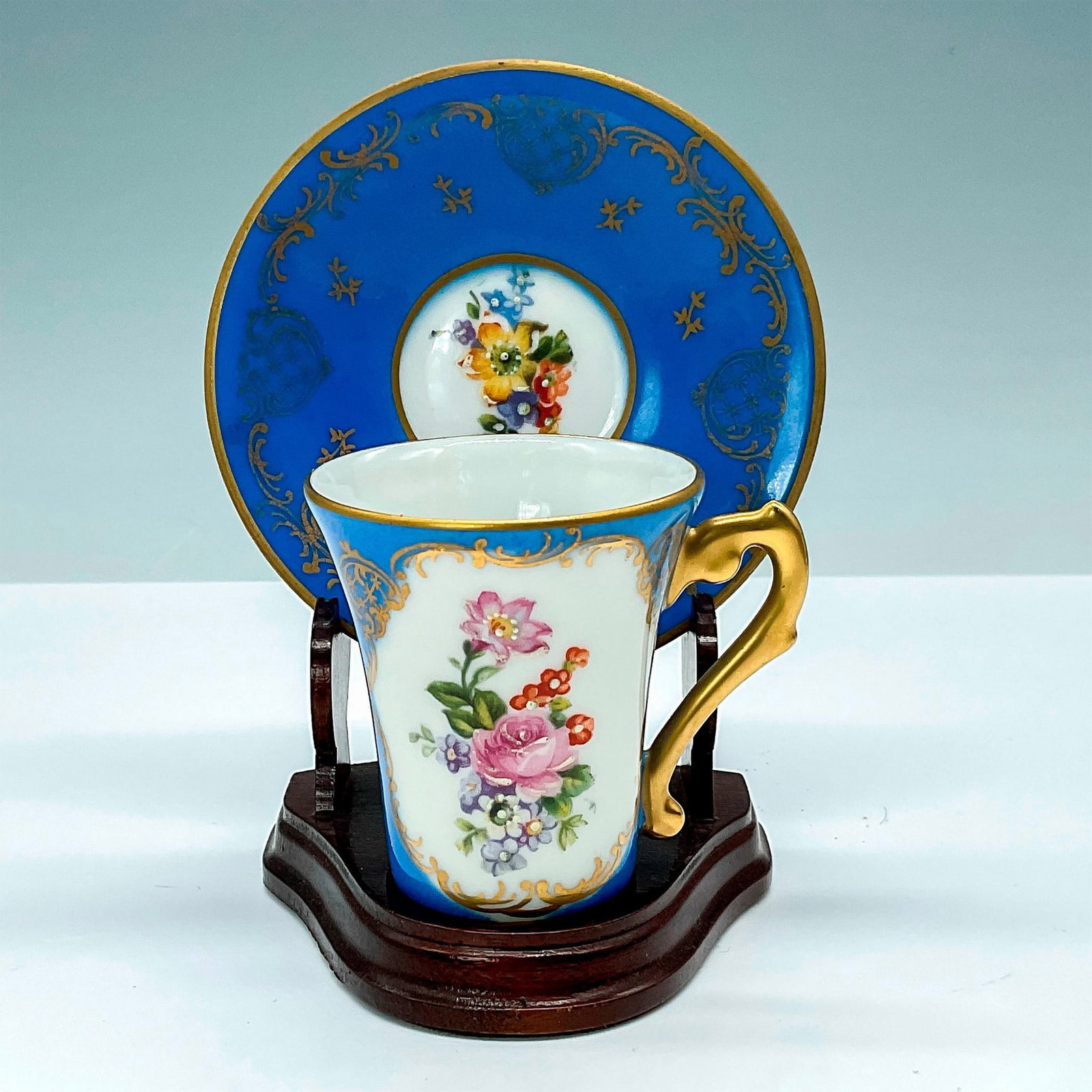 Limoges Porcelain Demitasse Cup and Saucer: Hand painted demitasse cup and saucer decorated in blue with floral motif embellished with gold gilt. Marked Hand Painted Pate de Limoges France to base. Cup measures: 2.75"L x 2.25"W x 2.5"H. Saucer 