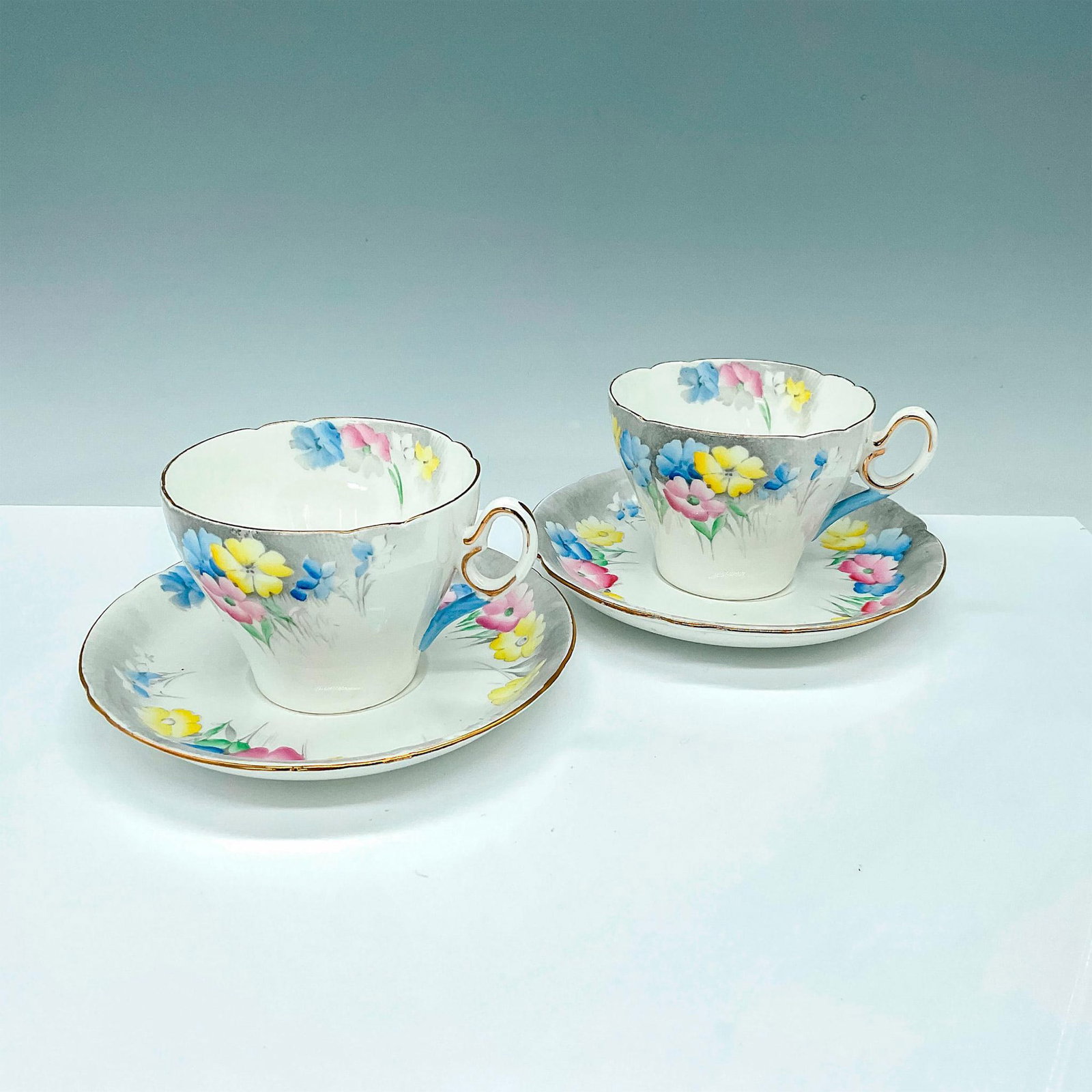 4pc Shelley China Teacups and Saucers Pattern 823343: 2 beautiful white bone china teacups with matching saucers decorated with blue, yellow, pink flowers and gold trim. Shelley backstamps. Cup: 4.25"L x 3.5"W x 2.75"H. Saucer: 1"H x 5.75"dia. Issued: 20