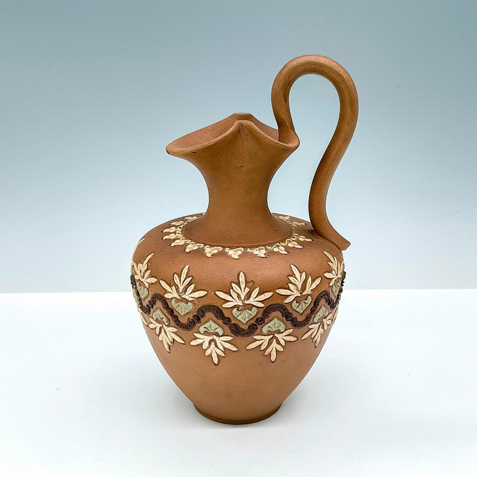 Royal Doulton Silicon Ware Ewer: The ewer features a fluted rim and a gracefully arched handle. Its body is adorned with intricate blue and white flowers and a rich chocolate brown serpentine line. A ring of delicate white leaves enc