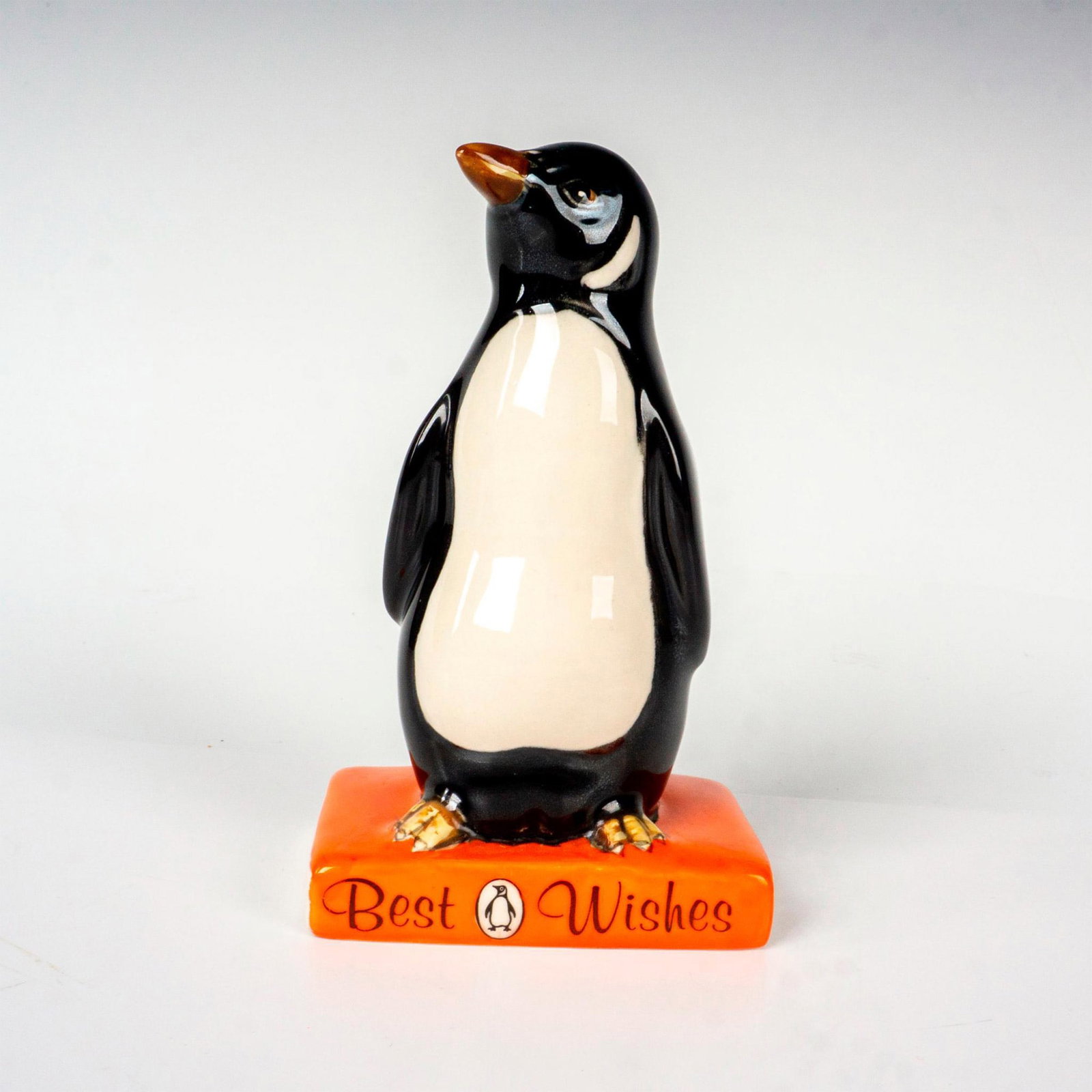 Best Wishes - Royal Doulton Advertising Figurine: Advertising model for the British publishing house Penguin Books. Penguin standing on an orange book. Royal Doulton backstamp. Issued: c. 1985 Dimensions: 2.75"L x 1.75"W x 4.75"H Manufacturer: Royal 
