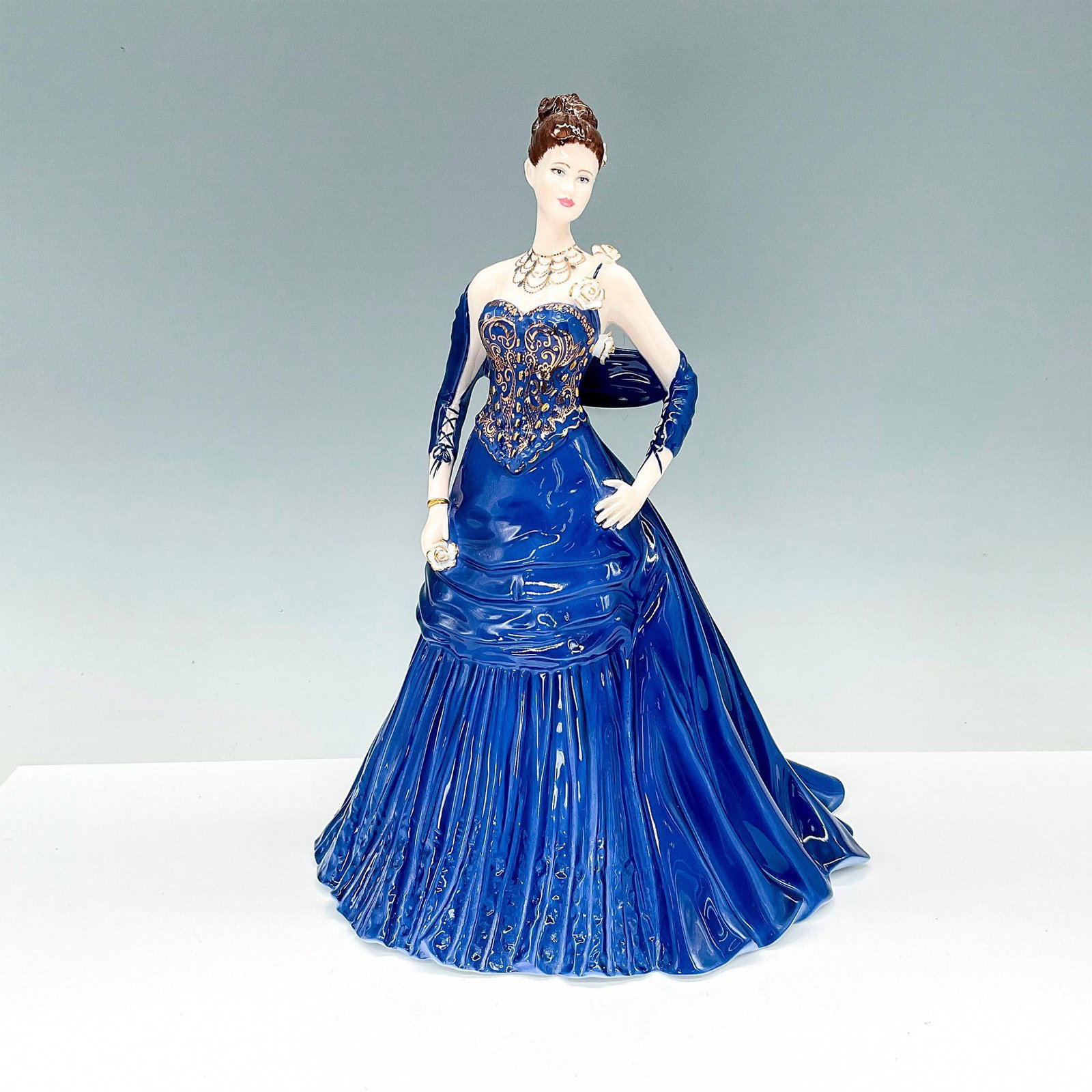 Coalport Porcelain Figurine, A Royal Engagement: This breathtaking porcelain figurine portrays a lady dressed in a stunning royal blue gown adorned with a beautifully embroidered gold bodice, exuding an aura of elegance and refinement. Commissioned 