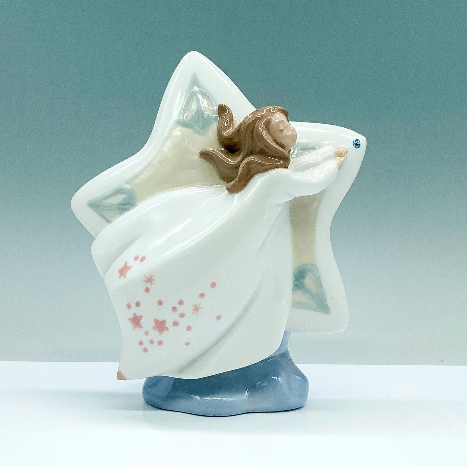 Nao by Lladro Porcelain Figurine, Shooting Star 1394: A glazed figure depicting a star with a floating woman in a white dress passing the center of the star. Nao by Lladro backstamp. Artist: Begona Jauregui Issued: 2000 Dimensions: 5.5"L x 3.25"W x 7"H M