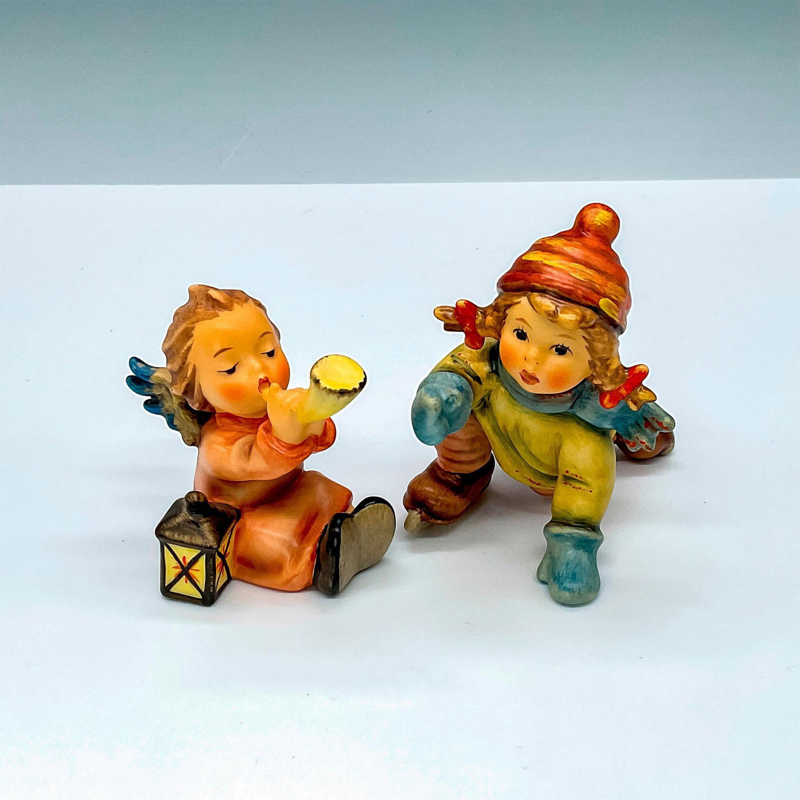 2pc Goebel Hummel Figurines, Tuneful Angel & Skating Lesson: 2 charming porcelain figurines, Tuneful Angel HUM359 and Skating Lesson HUM2058. Goebel backstamp. Largest piece measures 3.5"L x 2.5"W x 3.25"H. Manufacturer: Goebel Hummel Country of Origin: Germany