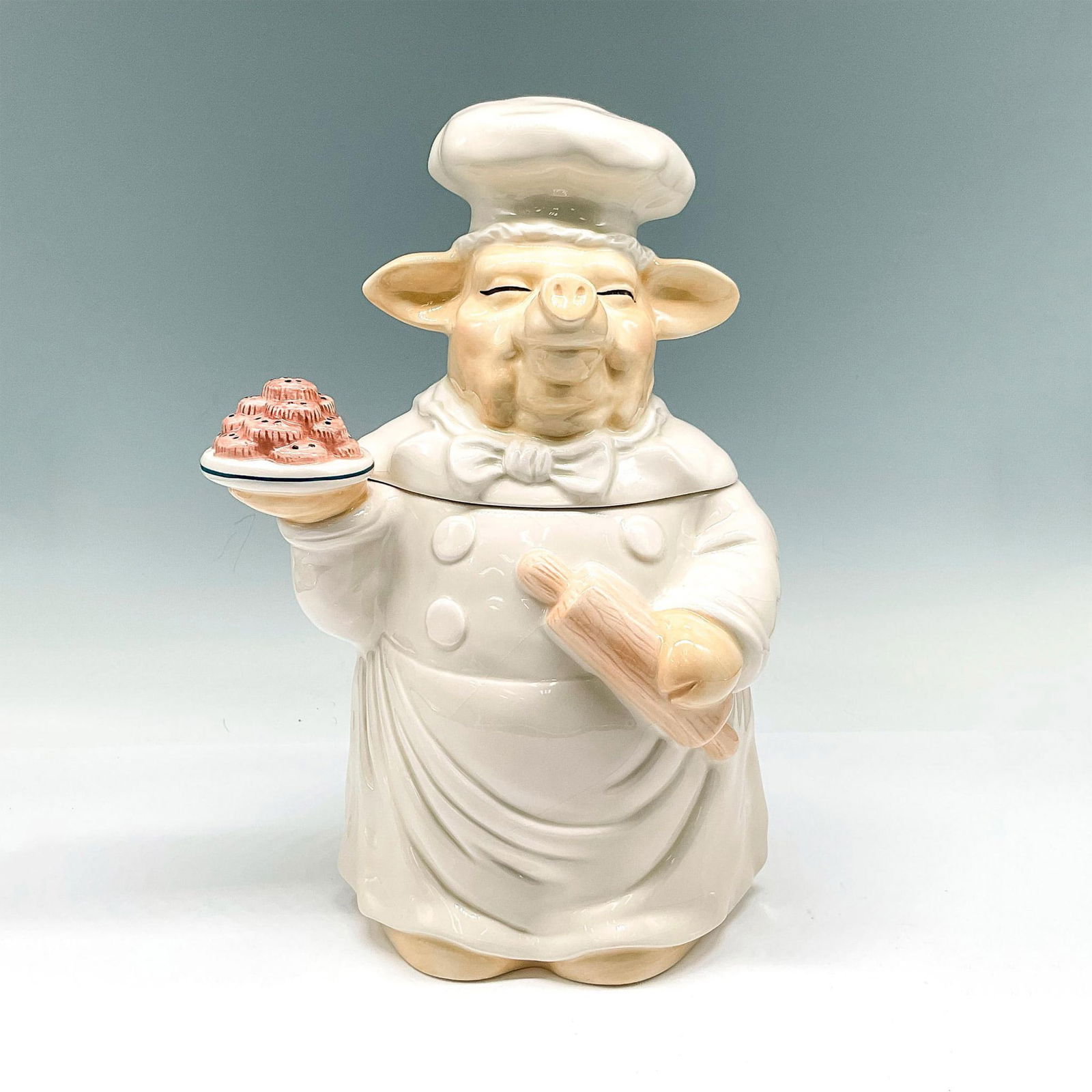 Cooks Club Porcelain Cookie Jar, Pastry Chef Pig: This endearing design with a happy chef holding a plate of goodies along with his rolling pin will make you smile. Colored in cream and white. Cooks Club backstamp. Issued: 20th century Dimensions: 7.