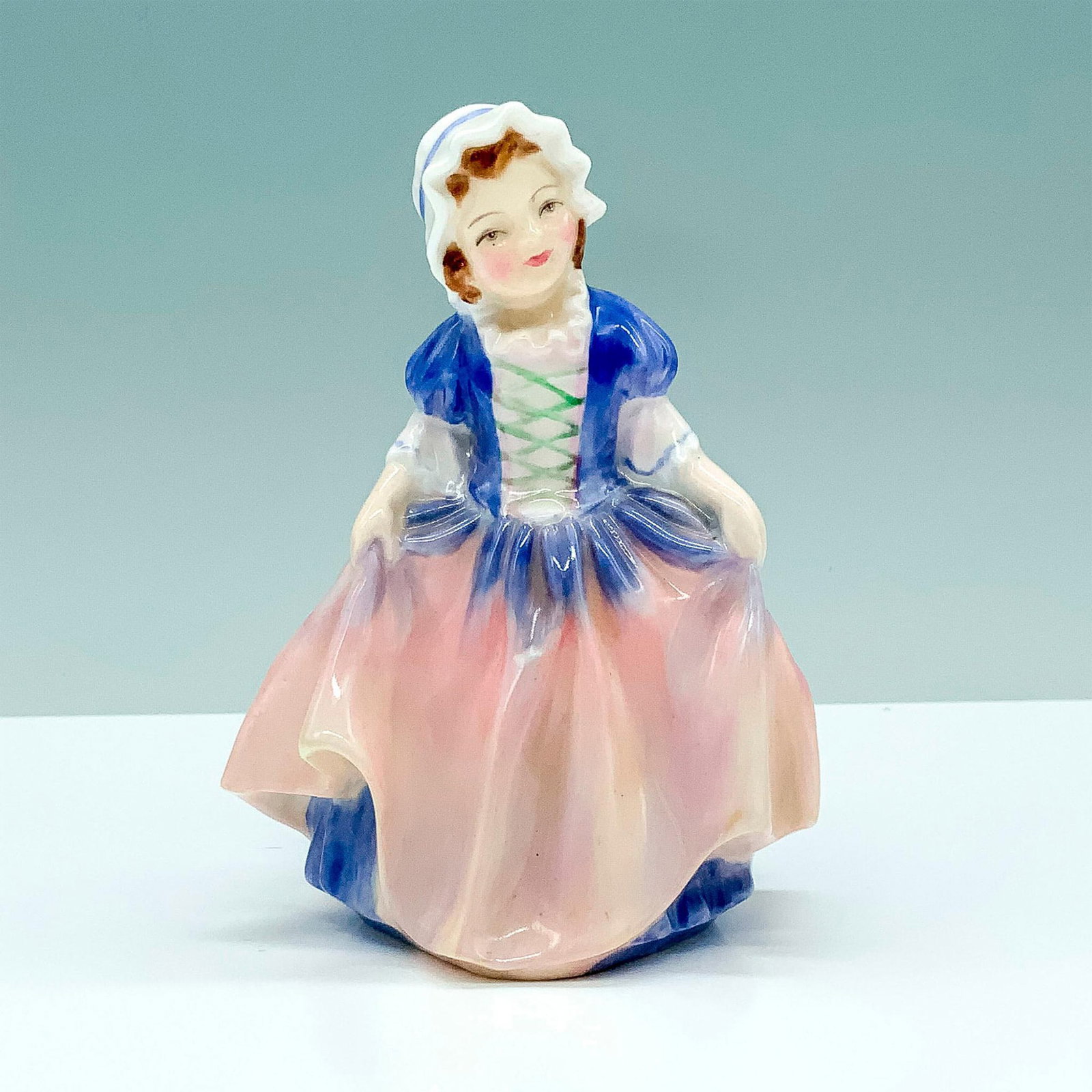 Dinky Doo HN1678 - Royal Doulton Figurine: A figure of a young girl in a blue and pink colored dress holding her skirt at her sides to bow. Royal Doulton backstamp. Dimensions: 3.5"L x 2.5"W x 4.75"H Manufacturer: Royal Doulton Country of Orig