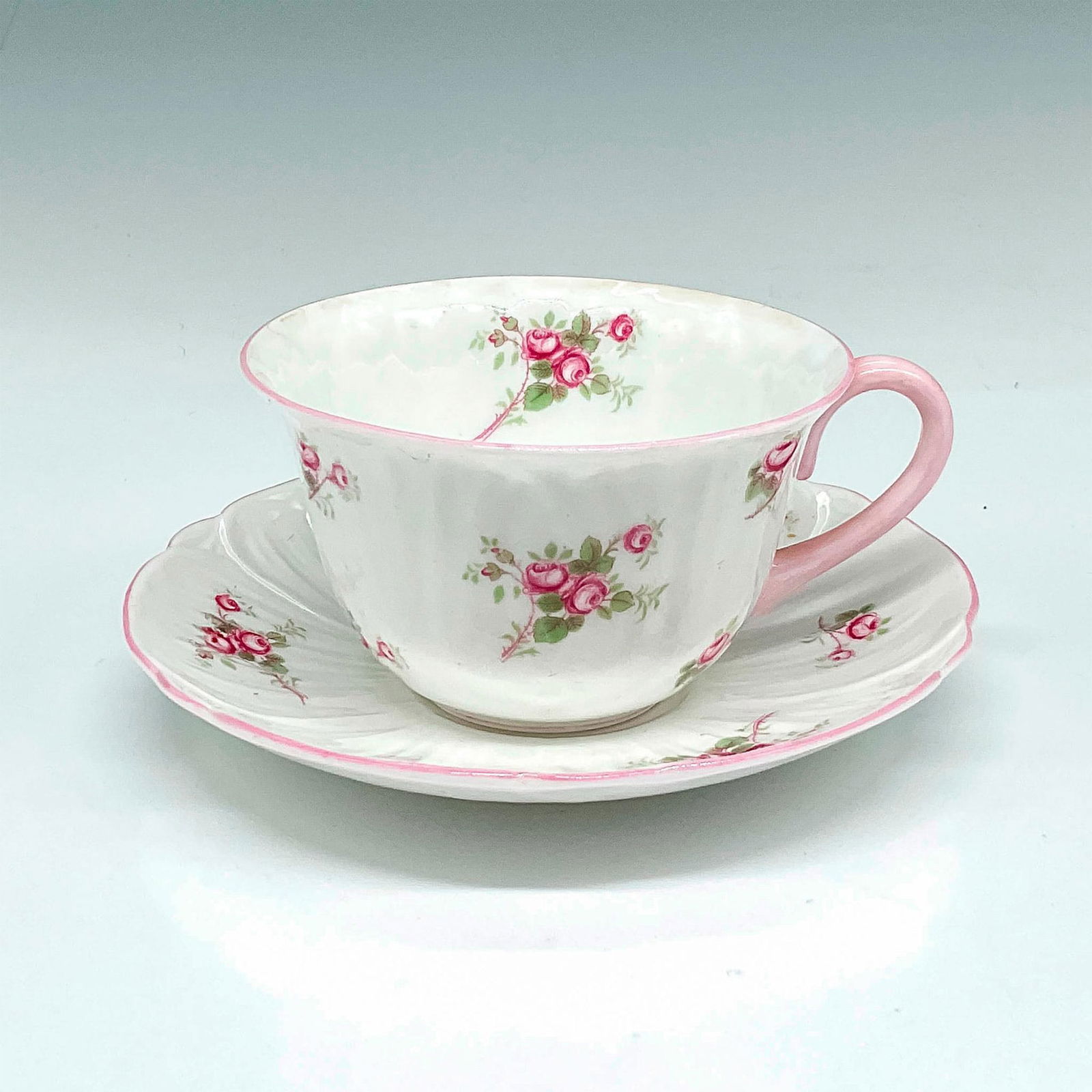 2pc Shelley Bone China Teacup and Saucer, Bridal Rose: Simple, elegant design of roses set on white background with pink rim and handle. Set includes teacup 2.5"H x 4"dia. and saucer 1"H x 5.5"dia. Shelley England backstamp. Issued: 20th century Manufactu