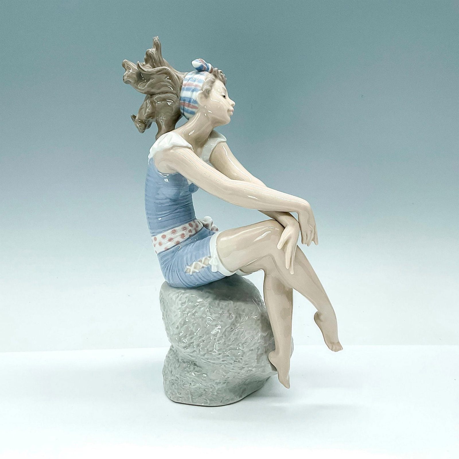Bathing Beauty 1005615 - Lladro Figurine: Depicts young girl sitting on a rock wearing a bathing suit. Lladro backstamp. Artist: Regino Torrijos Issued: 1989-1991 Dimensions: 6"L x 3.75"W x 10"H Manufacturer: Lladro Country of Origin: Sp