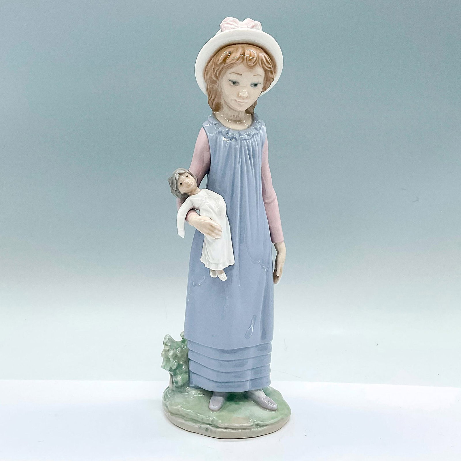 Belinda With Her Doll 1005045 - Lladro Porcelain Figurine: A glossy figure of a young girl holding her doll. Lladro backstamp. Artist: Vincente Martinez Issued: c. 1980-1995 Dimensions: 4"L x 3.75"W x 11.25"H Manufacturer: Lladro Country of Origin: Spain