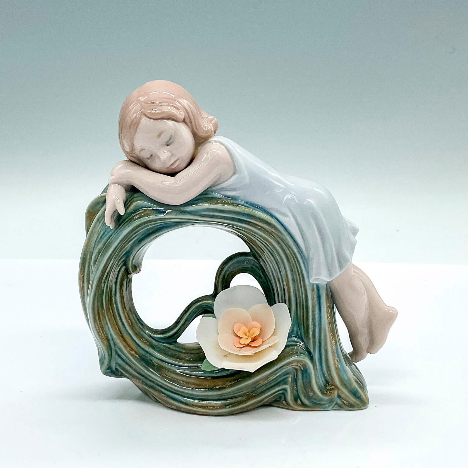 Childhood Dream 1008129 - Lladro Porcelain Figurine: A beautiful glossy figure of a young girl sleeping on a blue-green twisted grass with a peach-colored flower. Lladro backstamp. Artist: Marco Antonio Nogueron Issued: c. 2005-2009 Dimensions: 5.25"L x