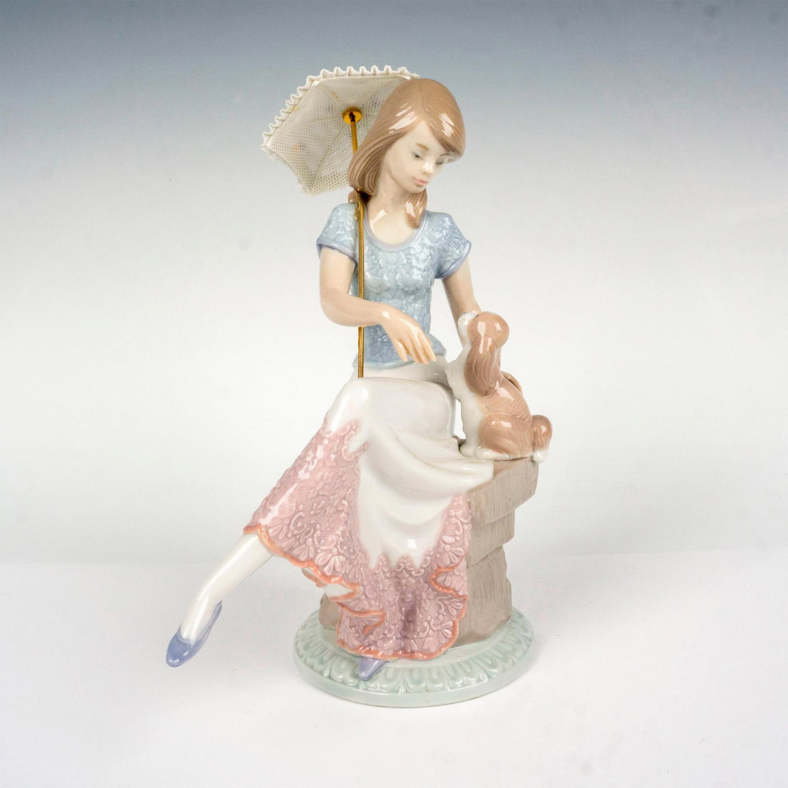 Picture Perfect 1007612 - Lladro Figurine: Porcelain Figurine of young girl sitting with her dog and a parasol in hand. Lladro backstamp. This item has its original box which measures: 13"L x 10"W x 6". Artist: Juan Huerta Issued: 1991 Dimensi