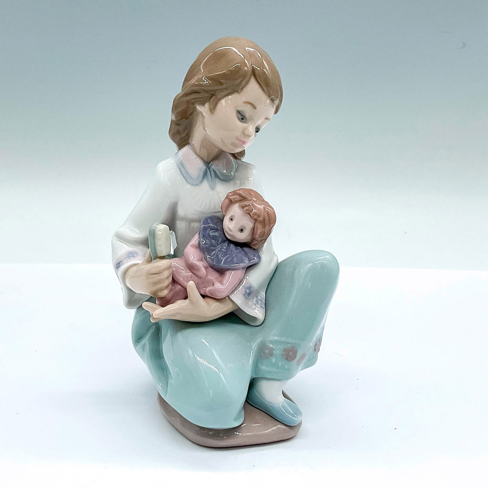 Thoughtful Caress 1005990 - Lladro Porcelain Figurine: A glossy figure of a young girl brushing her doll's hair. Lladro backstamp. Artist: Francisco Polope Issued: c. 1993-1196 Dimensions: 5"L x 3.25"W x 5.75"H Manufacturer: Lladro Country of Origin: