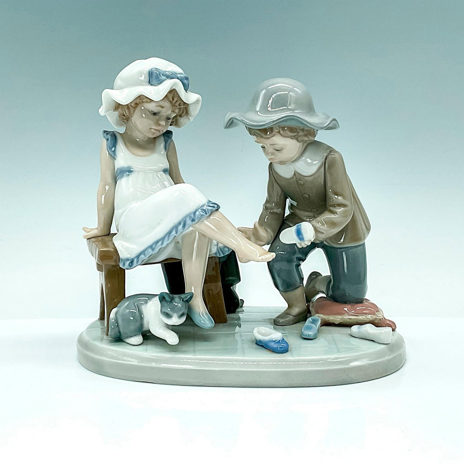 Try This One 1005361 - Lladro Figurine: Little boy helping little girl try on shoes while cat looks on. Lladro backstamp. Artist: Regino Torrijos Issued: 1986-1997 Dimensions: 6.75"L x 4.5"W x 6"H Manufacturer: Lladro Country of Origin: