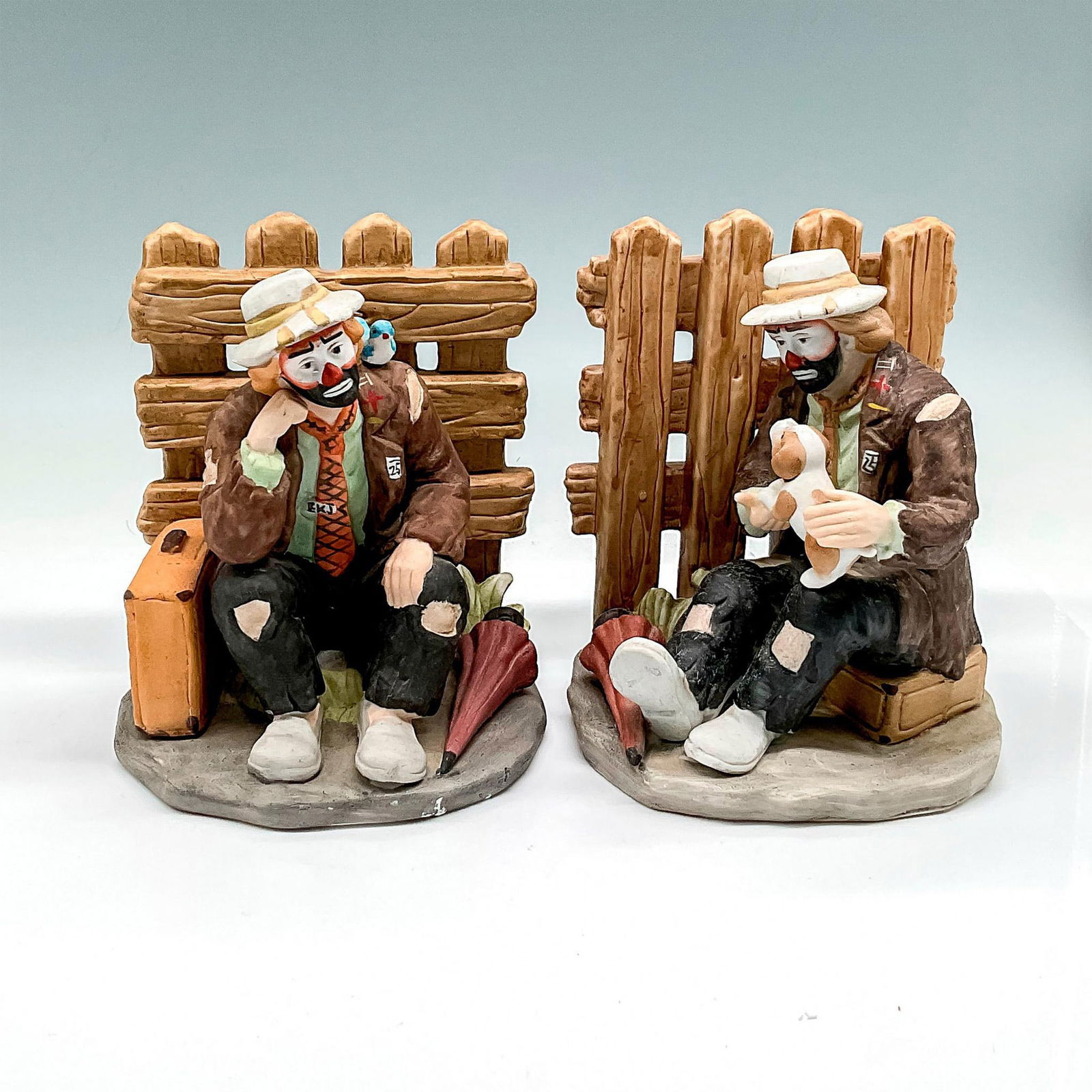 Flambro Imports Porcelain Bookends, Emmett Kelly, Jr.: Part of the EKJ Collectibles, Picket fence background with Emmett, bird and suitcase and on the other Emmett, dog and a umbrella. Signed. Flambro Imports backstamp and sticker. This item has its origi