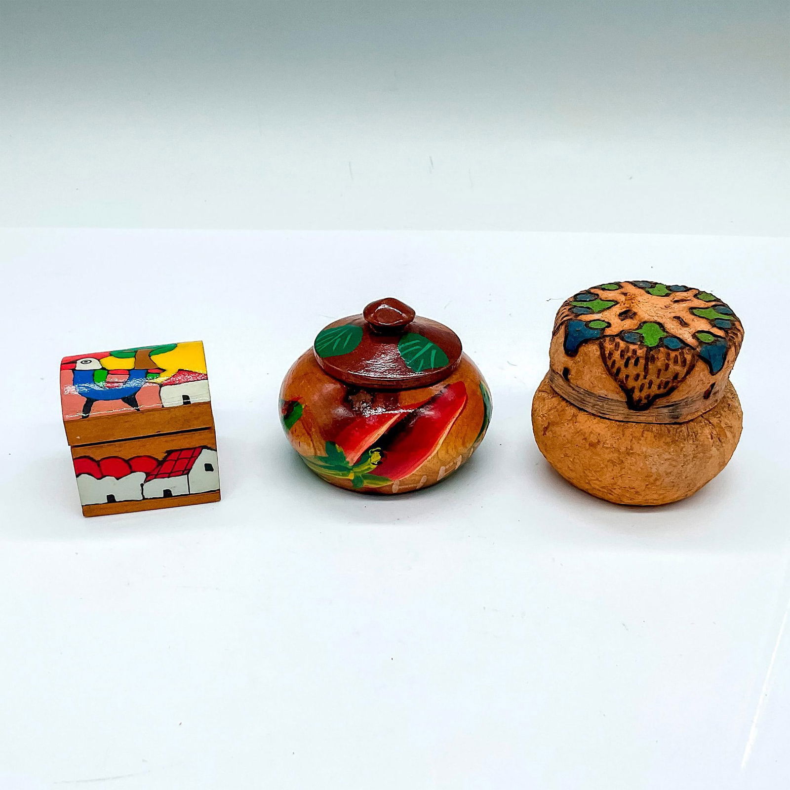 3pc Vintage Painted Wooden Decorative Boxes: Includes an adorable Salvadoran style tiny hinged covered box with a colorful toucan. A Haitian hand painted box with a red hibiscus. An Uruguayan hand carved box with blue and green pattern on the li