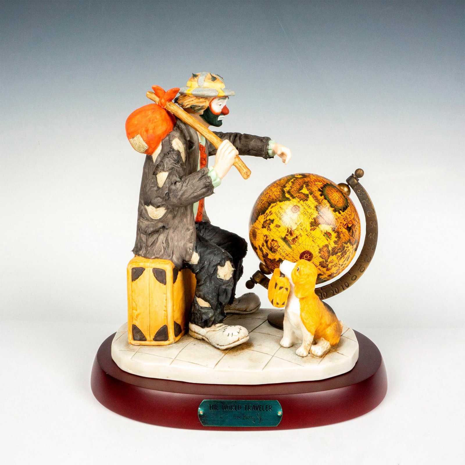 Flambro Emmett Kelly Jr. Figurine, The World Traveler: Limited edition, hand painted bisque porcelain depicting Weary Willy the clown deciding where he will go next with his travel buddy, the dog. Rests on a wooden base with gold-tone titled plaque. Emmet