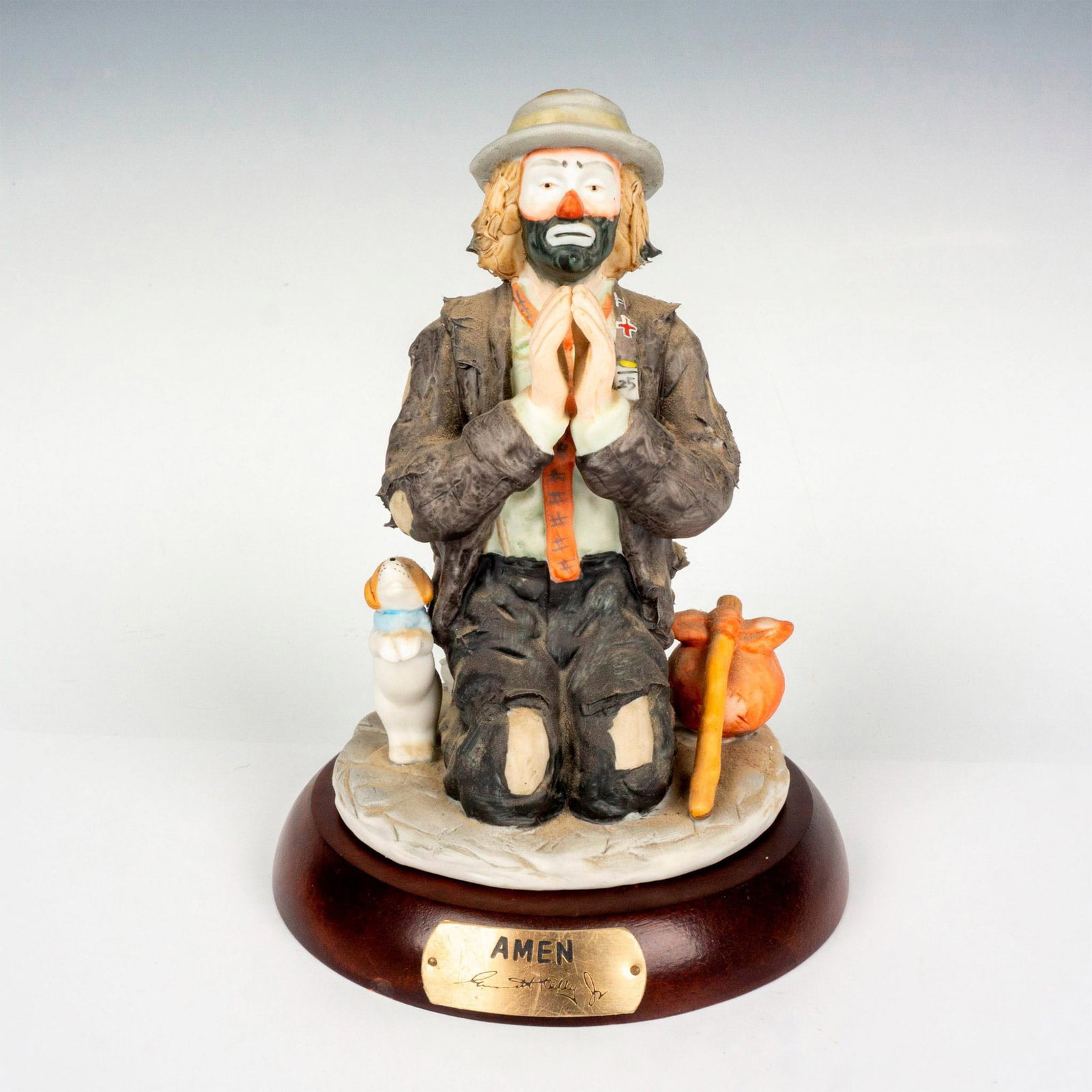 Flambro Emmett Kelly Jr. Figurine, Amen: Limited edition, hand painted bisque porcelain depicting figural clown Weary Willie in prayer position with pup by his side. Rests on a wooden base with gold-tone titled plaque. Emmett Kelly Jr. signa