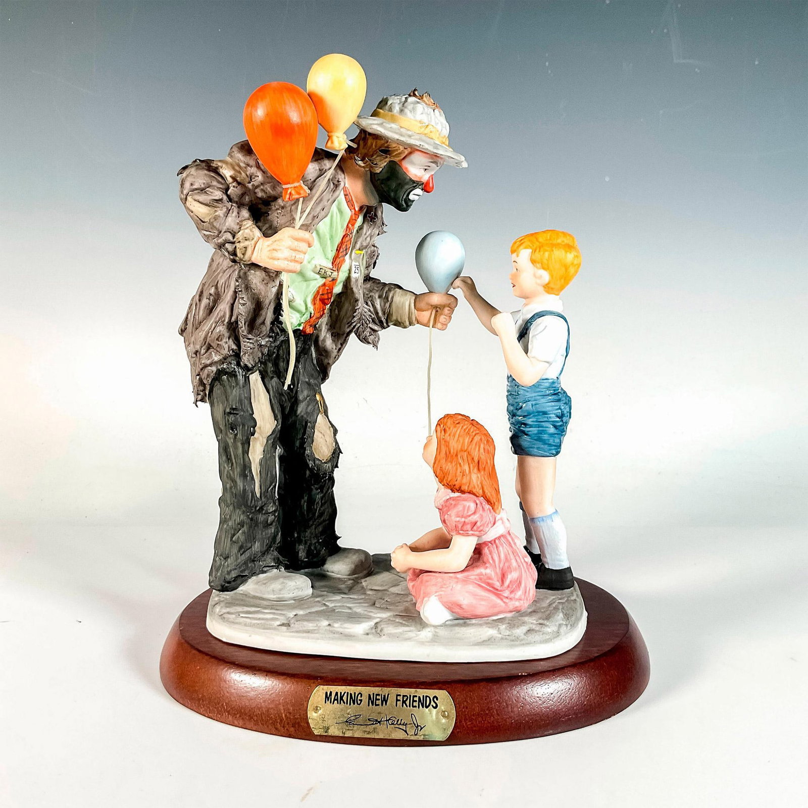 Flambro Emmett Kelly Jr. Figurine, Making New Friends: Limited edition, hand painted bisque porcelain depicting figural clown Weary Willie giving balloons to children. Rests on a wooden base with gold-tone titled plaque. Emmett Kelly Jr. signature backsta