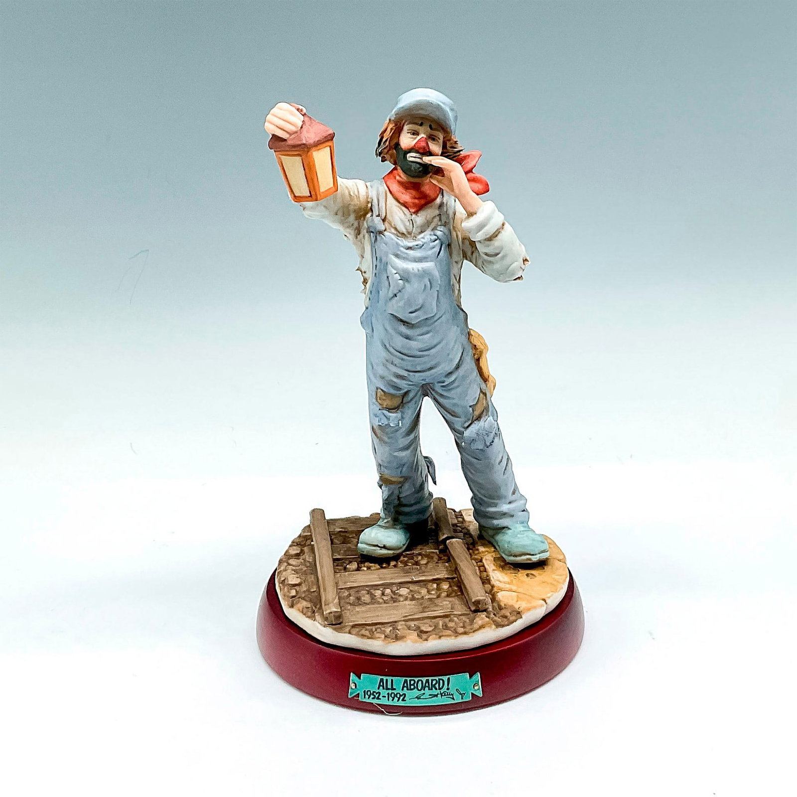 Flambro Imports Figurine, Emmett Kelly, Jr. All Aboard + Base: Dressed in overalls, holding lantern, calling out. Signed. No. 1044. Flambro Imports backstamp. This item has a base included: 0.75"H x 5"dia. Issued: 1952 - 1992 Dimensions: 8"H x 4.25"dia. Manufactu