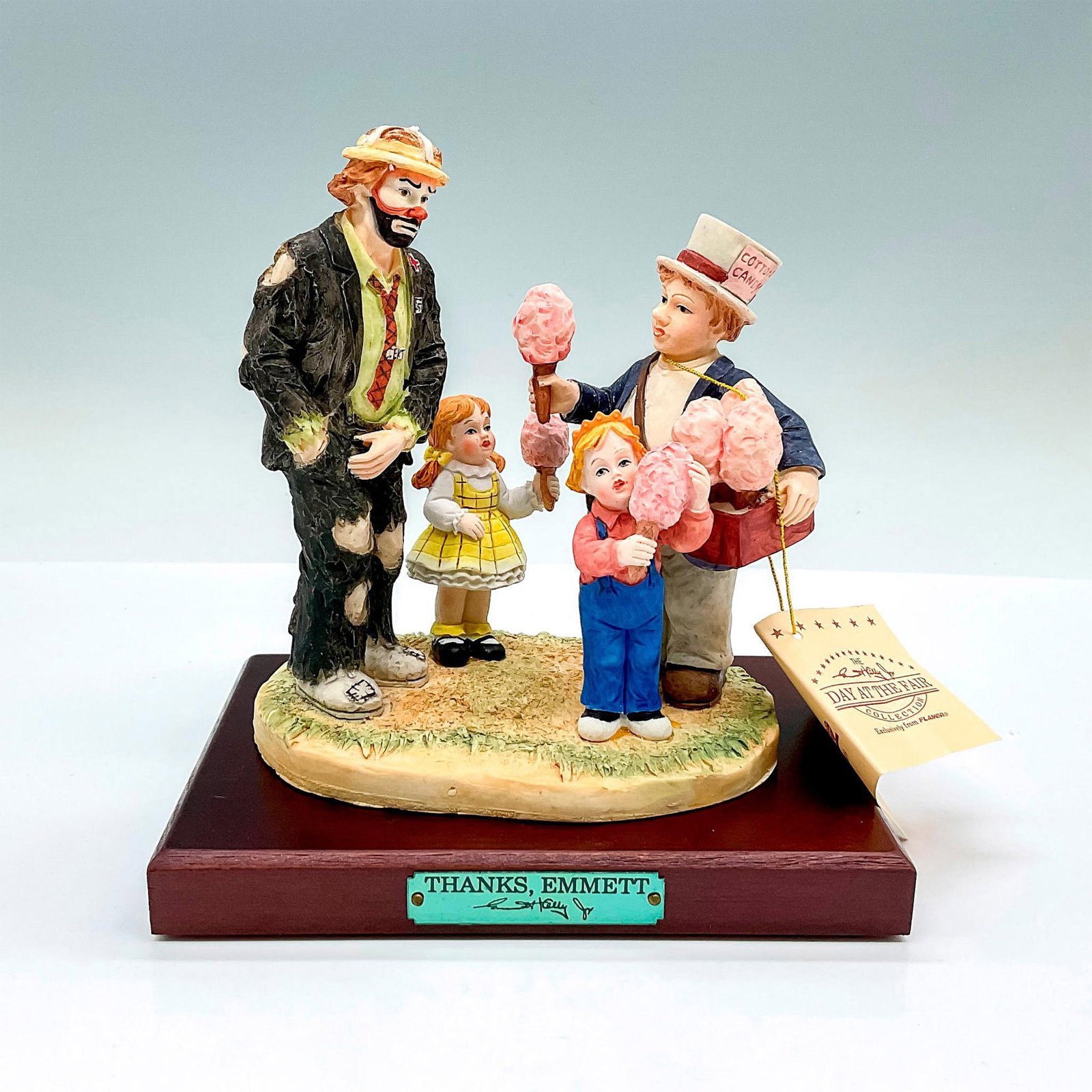 Flambro Emmett Kelly Jr. Figurine, Thanks, Emmett: Part of the Day At The Fair Collection. Limited issue 1723. Hand painted porcelain figure. Depicting Emmett the clown paying for the children's cotton candy. Sits on a wooden base with gold-tone title