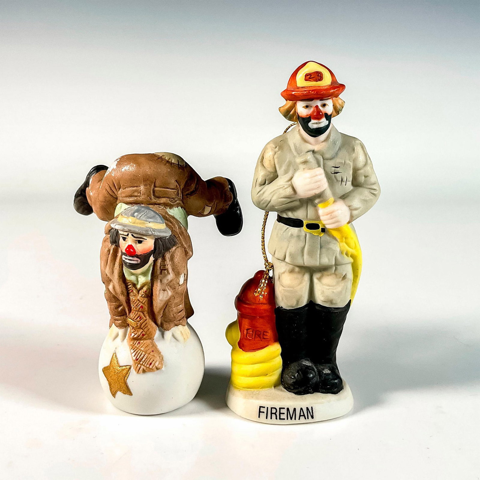 2pc Flambro Emmett Kelly Jr. Figurine and Christmas Ornament: Hand painted bisque porcelain ornament titled Fireman and figurine modeled as Weary Willie balancing on a ball. Emmett Kelly Jr. backstamp. Flambro backstamp. Ornament measures: 2"L x 1.5"W x 4.75"H. 