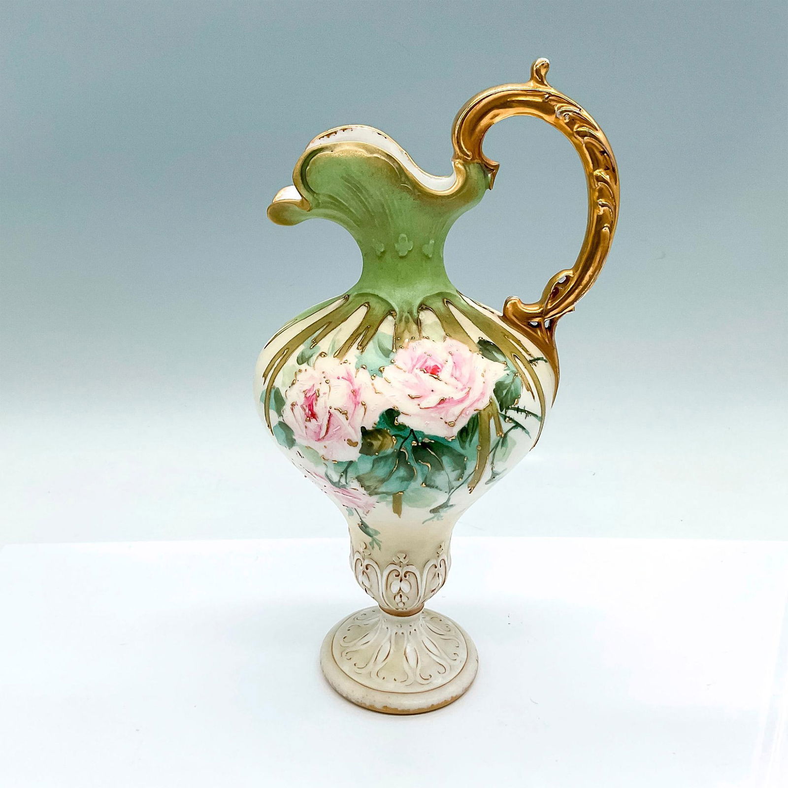 Amphora RStK Floral Ewer: A stunning green and cream-colored pitcher with a gilded handle. Hand painted with pink roses and gilded accents. Amphora RStK marked on the underside. Issued: c. 1982-1910 Dimensions: 5.5"L x 4.75"W