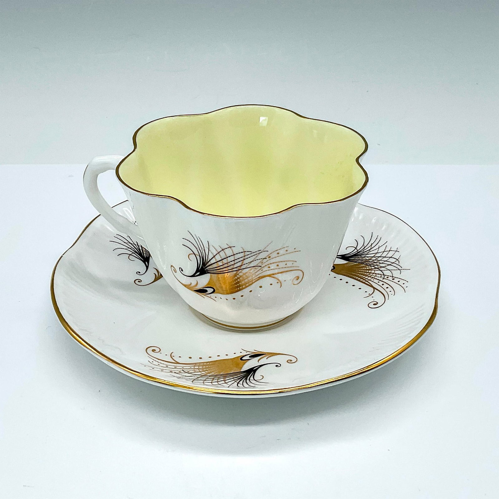 Shelley Bone China Teacup & Saucer Set, Gold Feathers: Dainty teacup and saucer set in the Caribbean pattern number 14092/S34, titled Gold Feathers, featuring an elegant combination of white, yellow, gold, and black. White teacup with yellow interior, gol