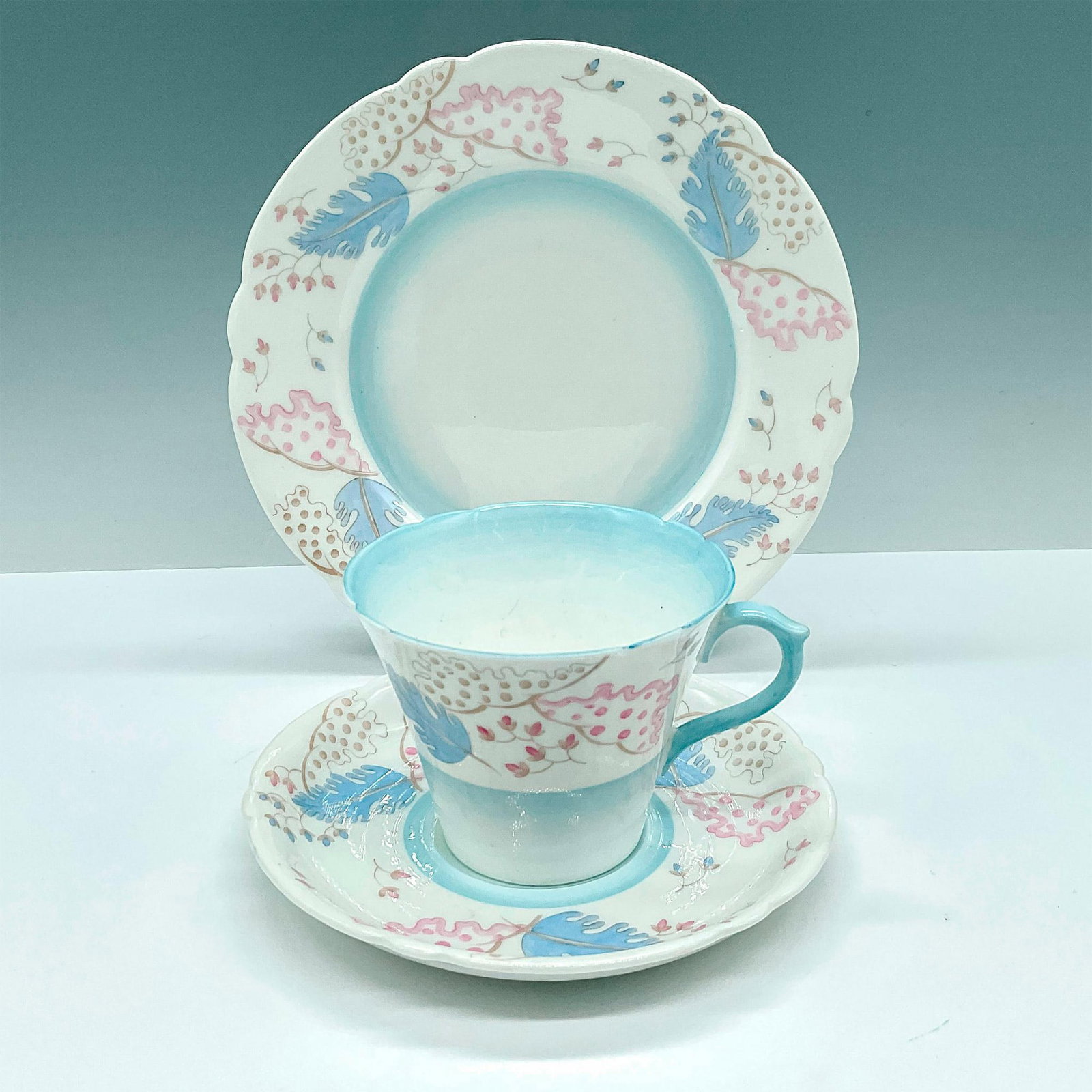 3pc Shelley Bone China Trio Tea Set, Pink & Blue Leaves: Dreamy teacup, matching saucer, and plate set of beautiful white china decorated with pink and blue leaves. Shelley backstamps. Cup: 4.25"L x 3.5"W x 2.75"H. Saucer: 1"H x 5.75"dia. Plate: 1"H x 7.25"