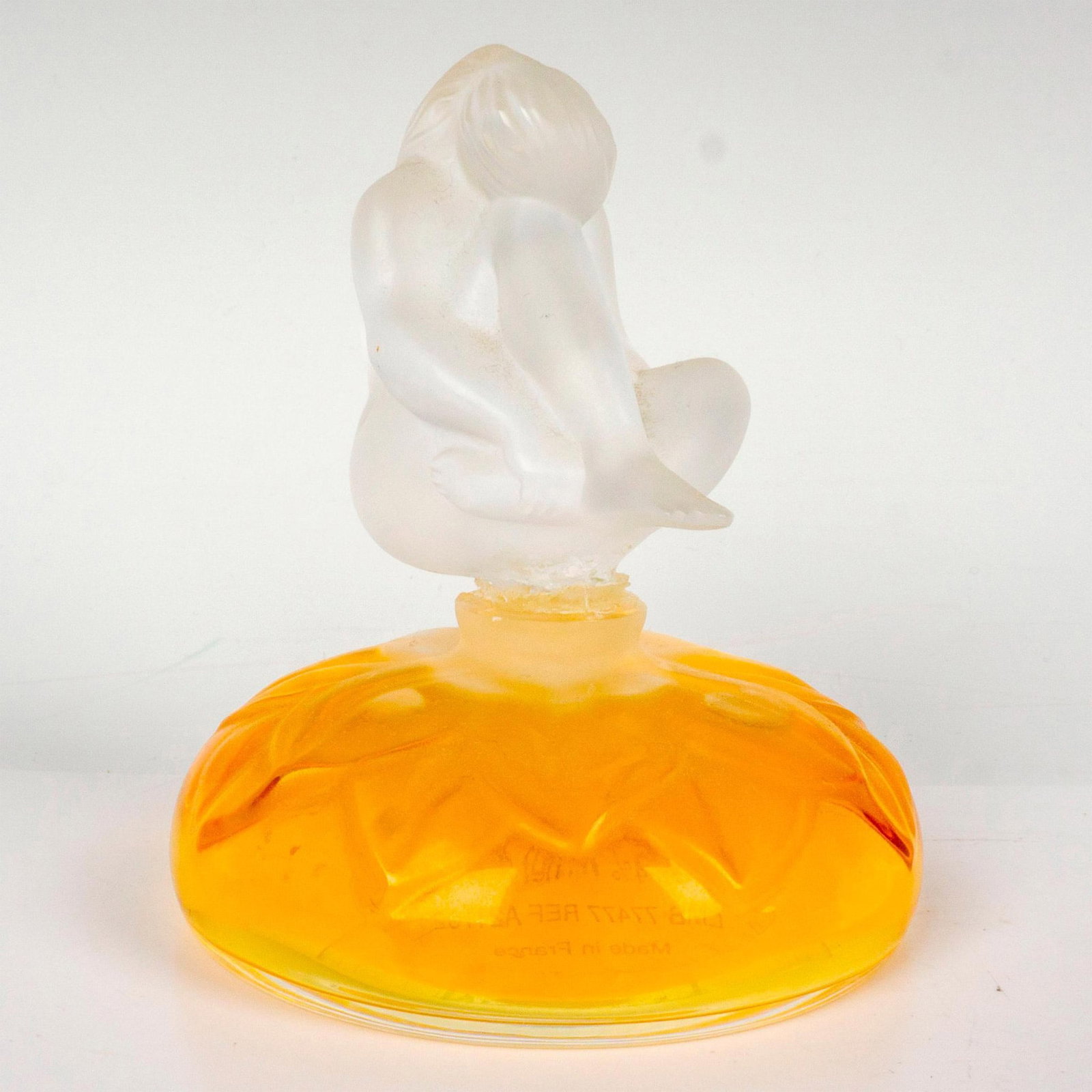 Lalique Crystal Perfume Bottle, Le Nu: Satin finish vessel embossed with foliage pattern. Includes a frosted crystal figural stopper depicting a nude woman with head on knee. Lalique factory label. Lalique France etched backstamp. Issued: 
