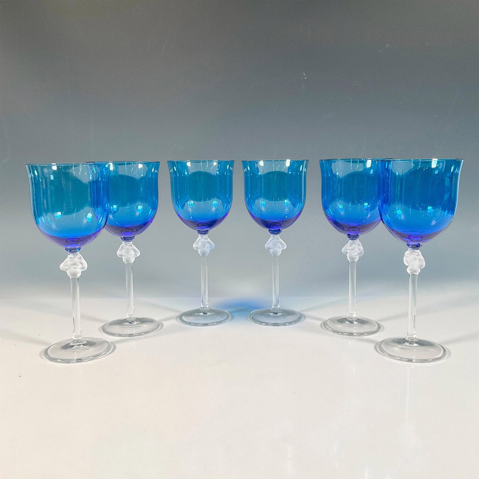 6pc Lalique Crystal, Blue Roxane Burgundy Wine Glasses: Six tall wine glasses with frosted piece at the top of the stem of two ladies wrapped around with grapes; blue bowl. Lalique etched mark. Dimensions: 7.5"H x 3" dia Manufacturer: Lalique Country of Or