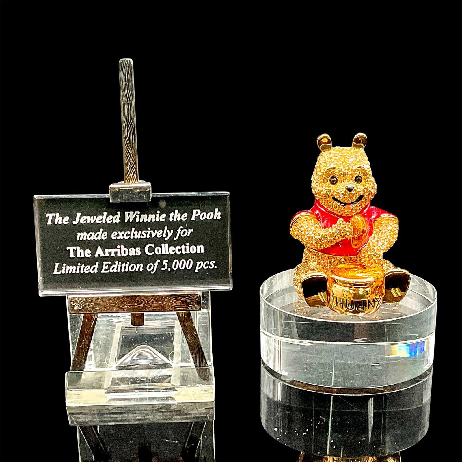 3pc Arribas Brothers Figurine, Winnie the Pooh, Sign + Base: Winnie the Pooh sits eating a bowl of honey covered in over 600 Swarovski Crystals. Included is a Swarovski plaque with its adorable display easel. This item has its original box which measures 3.75"L