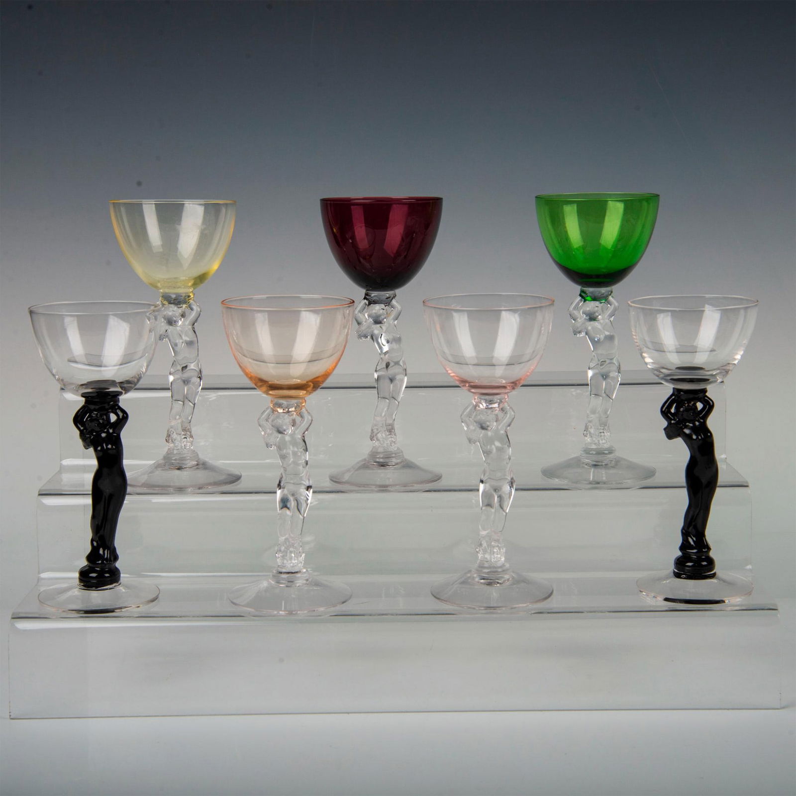 7pc Cambridge Crystal Liquor Cocktail Glasses, Nude Stem: Attractive, colorful set of cocktail glasses with amethyst, amber, gold krystol, forest green, and clear bowls. Stem is decorated with an Art Deco nude sculpture. Issued: 1931-1958 Dimensions: 2.75"W