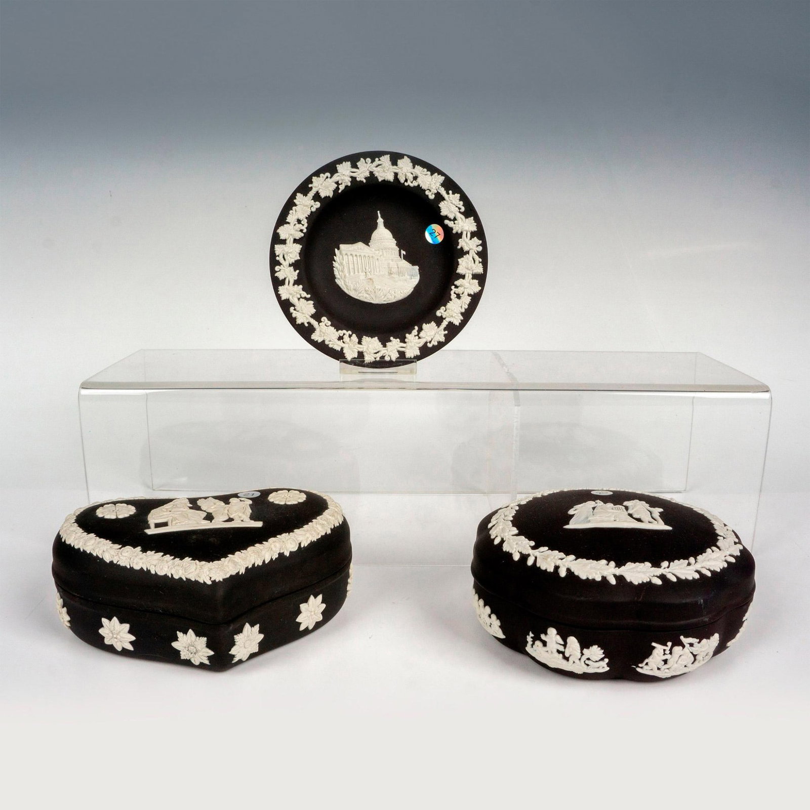 3pc Wedgwood Black Jasperware Collectibles: Includes a small round pin tray, a lidded heart shaped box, and a lidded round box. Decorated in a white relief with neoclassical figures surrounded by foliage patterns. Wedgwood backstamp. Tray measu