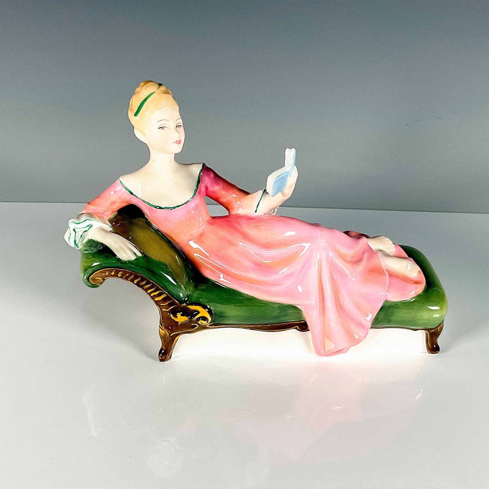 Repose - HN2272 - Royal Doulton Figurine: Peggy Davies Classics series. She wears a pink dress, reading a book, and relaxing on a green chaise lounge. Royal Doulton backstamp. Artist: Peggy Davies Issued: 1972 - 1979 Dimensions: 5.25"H Manufa