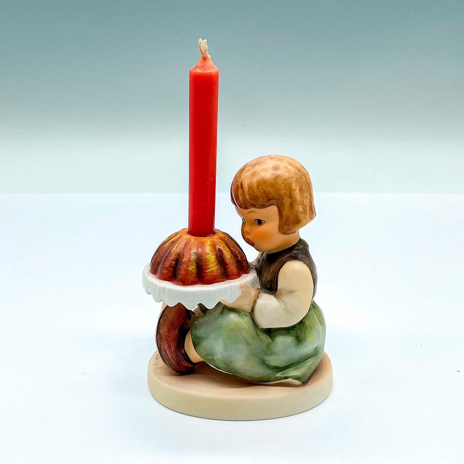 Goebel Hummel Porcelain Figurine, Birthday Cake HUM 338: Hand painted figure of a young girl holding a birthday Bundt cake. Red candle included. Goebel backstamp. Artist: M.I. Hummel Issued: 1997 Dimensions: 3"L x 2.25"W x 3.5"H Manufacturer: Goebel Hummel