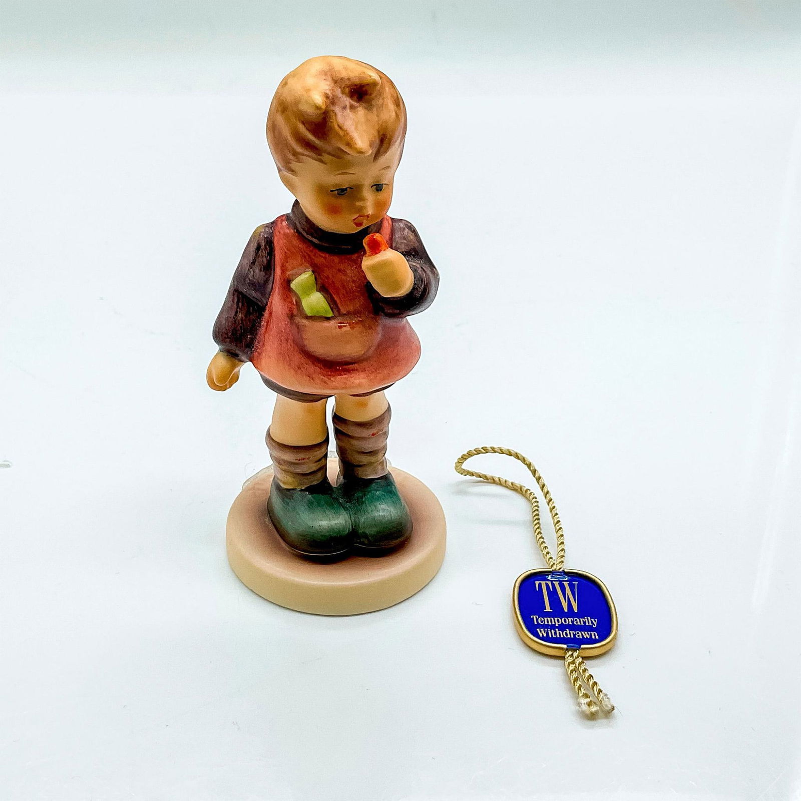 Goebel Hummel Porcelain Figurine, Delicious: First Issue 1996. Hand painted child with blue shoes eating a treat. Goebel backstamp. Impressed mark 435. Issued: 1996 Dimensions: 4"H x 1.75" dia. Manufacturer: Goebel Hummel Country of Origin: Germ