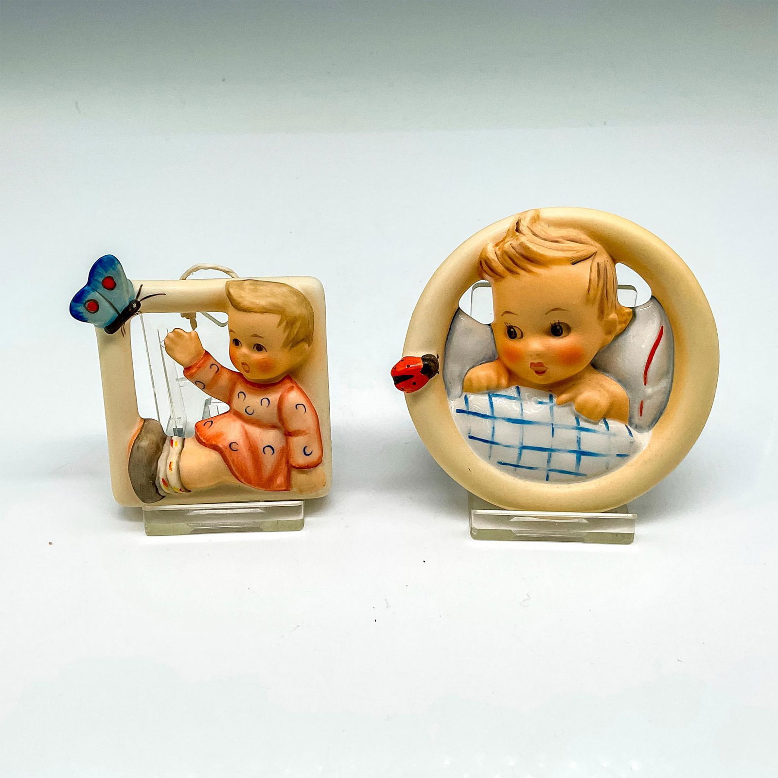 2pc Goebel Hummel Porcelain Wall Ornaments: Includes window design with little boy in center (139) 2"L x 2"W x 0.50"H and round baby in bed (137) 0.75"H x 3" dia. Goebel backstamp and Hummel impressed mark. Issued: 20th century Manufacturer: Go