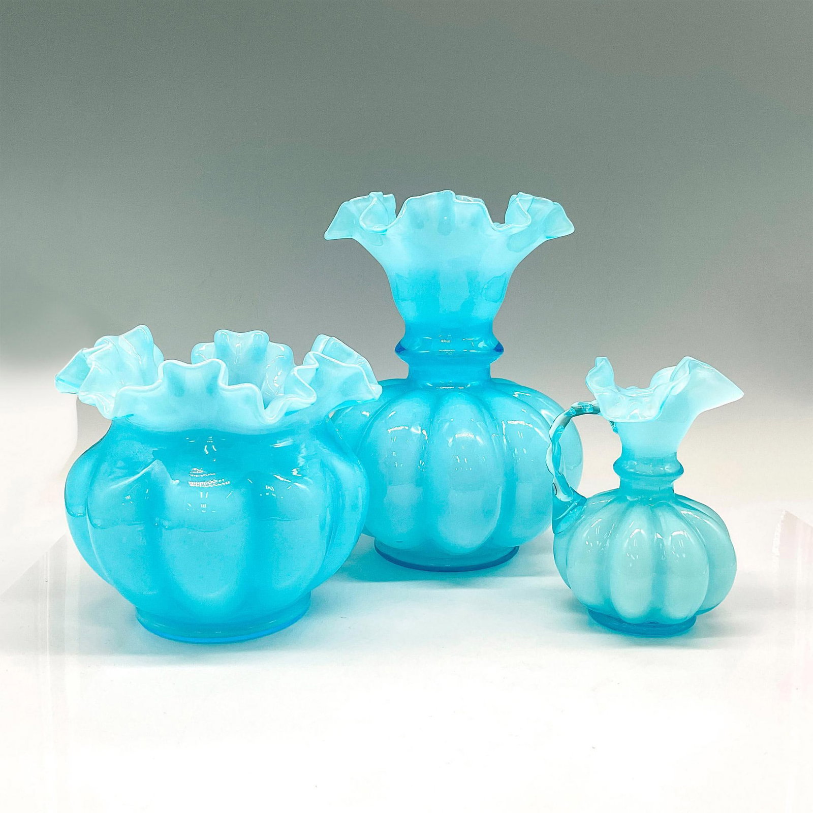 3pc Fenton Blue Double Crimped Melon Vase + Pitcher: Includes lovely large ruffled vase (8"H x 6" dia.), round bulb ruffled vase (5.5"H x 6" dia.) and small melon pitcher with ruffled edge and clear blue glass handle (5"H x 3.25" dia.). Largest piece: 8