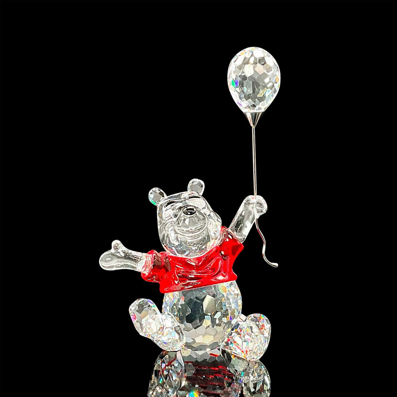 Swarovski Crystal Figurine, Winnie the Pooh: This piece sparkles in fully faceted clear crystal with unfaceted face and arms with eyes, nose, and eyebrows in Jet crystal. His shirt is in Light Siam crystal. He jumps around happily holding a clea