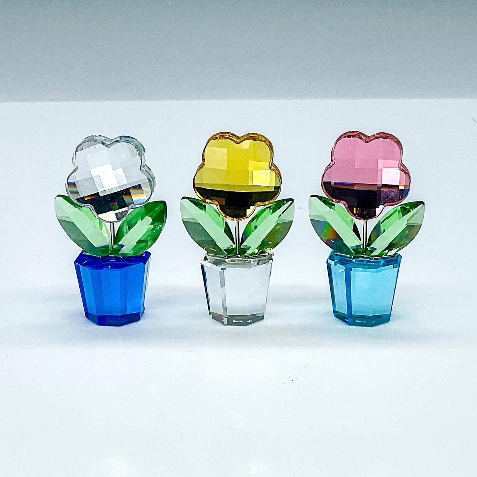 3pc Swarovski Crystal Flowers, Colored Sunflowers in Pots: Adorable flowers in yellow, white, and pink in blue and clear pots. Swarovski etched backstamp. Pot of clear faceted crystal. Leaves in green and yellow flower. These items each come with an original 