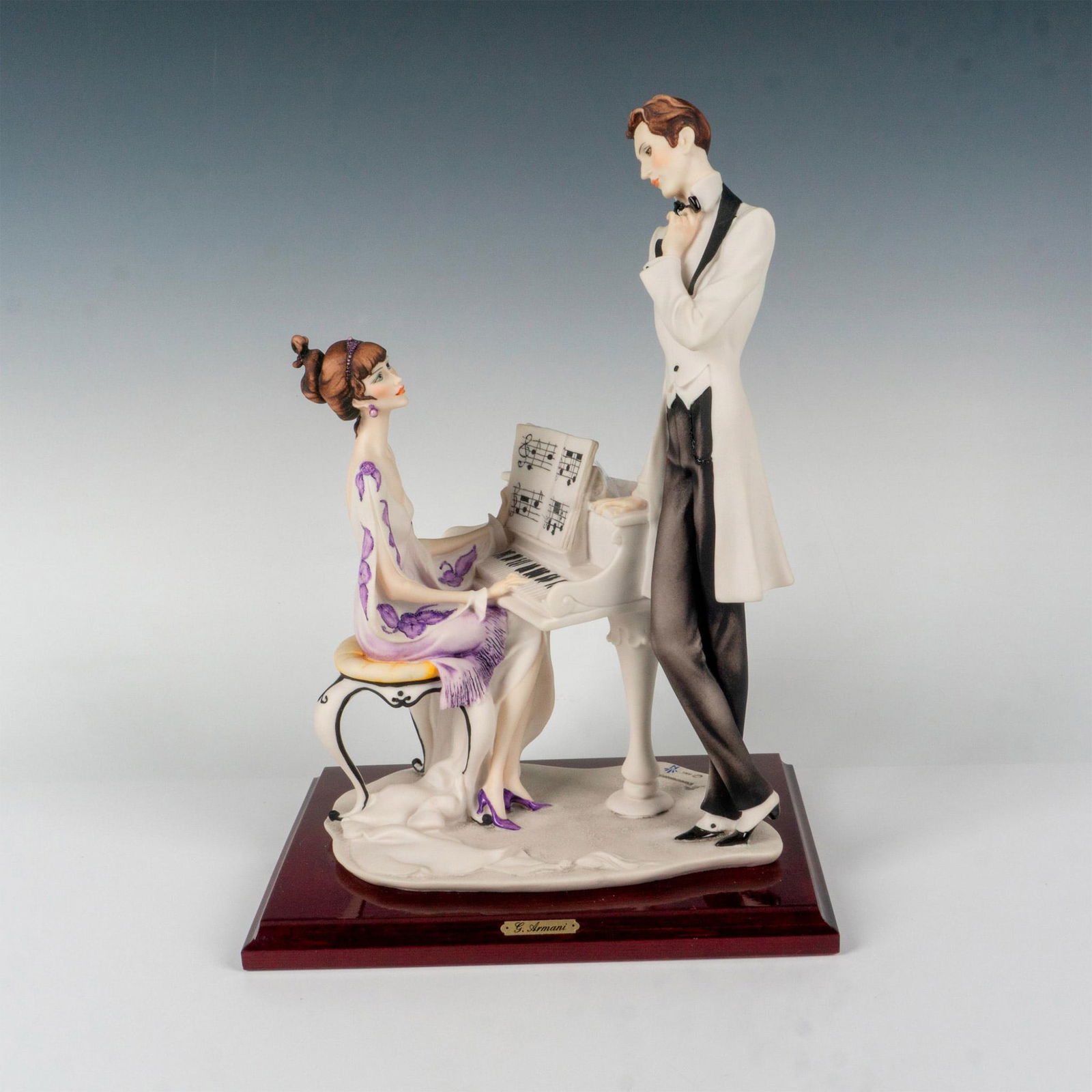 Florence Capodimonte Giuseppe Armani Figurine The Piano: Cream color matte figure of a lady in a white and purple dress seated at a piano. A finely dressed man stands leaning on the piano watching her. Florence and Capodimonte mark. Artist: Giuseppe Armani