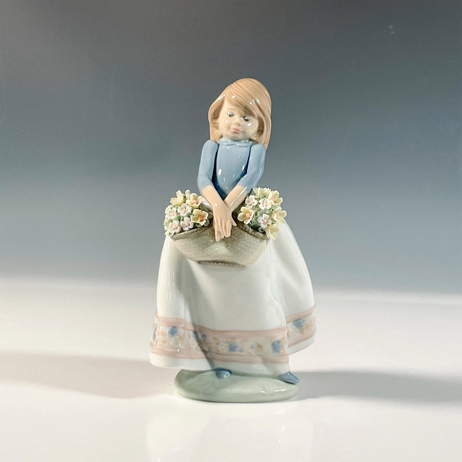 May Flowers 1005467 - Lladro Porcelain Figurine: Glossy finish; Lladro backstamp. Artist: Juan Huerta Issued: 1988 Dimensions: 6.75"H x 2.75"W Manufacturer: Lladro Country of Origin: Spain